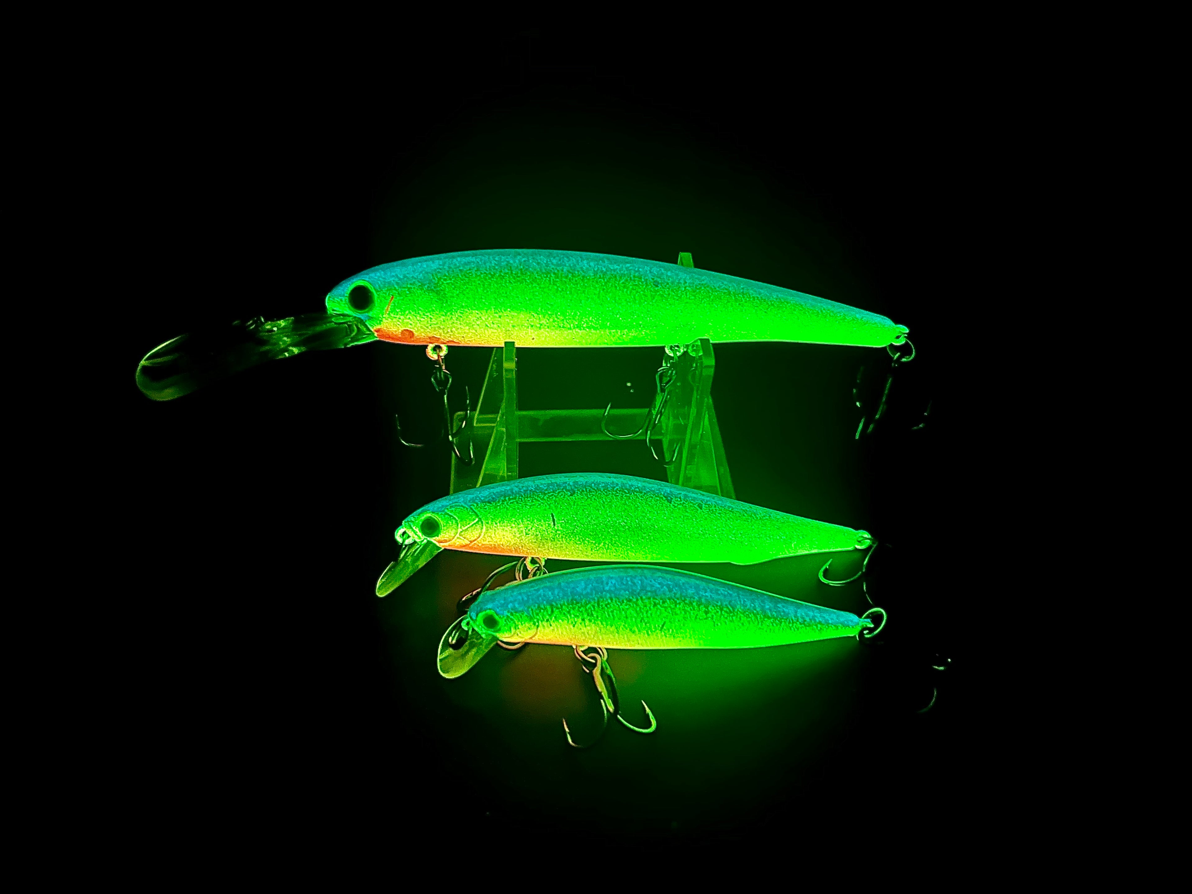 Three glowing jerkbait lures with green-blue bodies and orange belly, treble hooks.