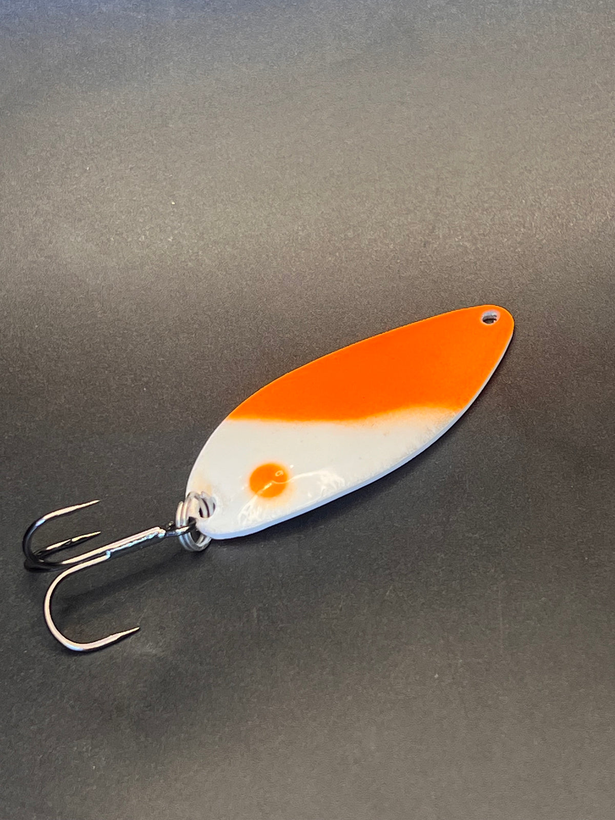 Orange-and-white casting spoon lure with treble hook, glossy finish