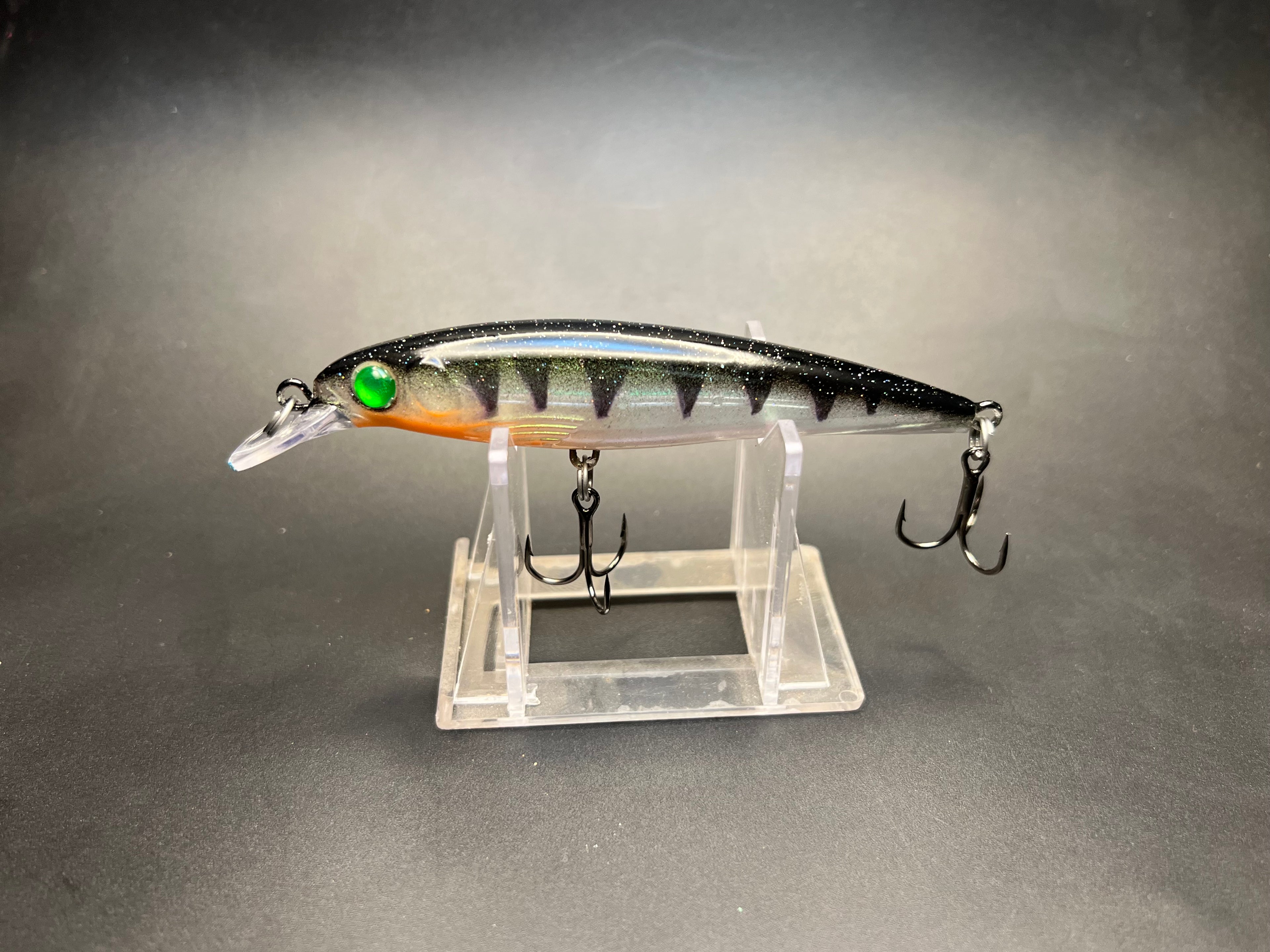 Fishing lure with black body, green eye, orange underside, and treble hooks