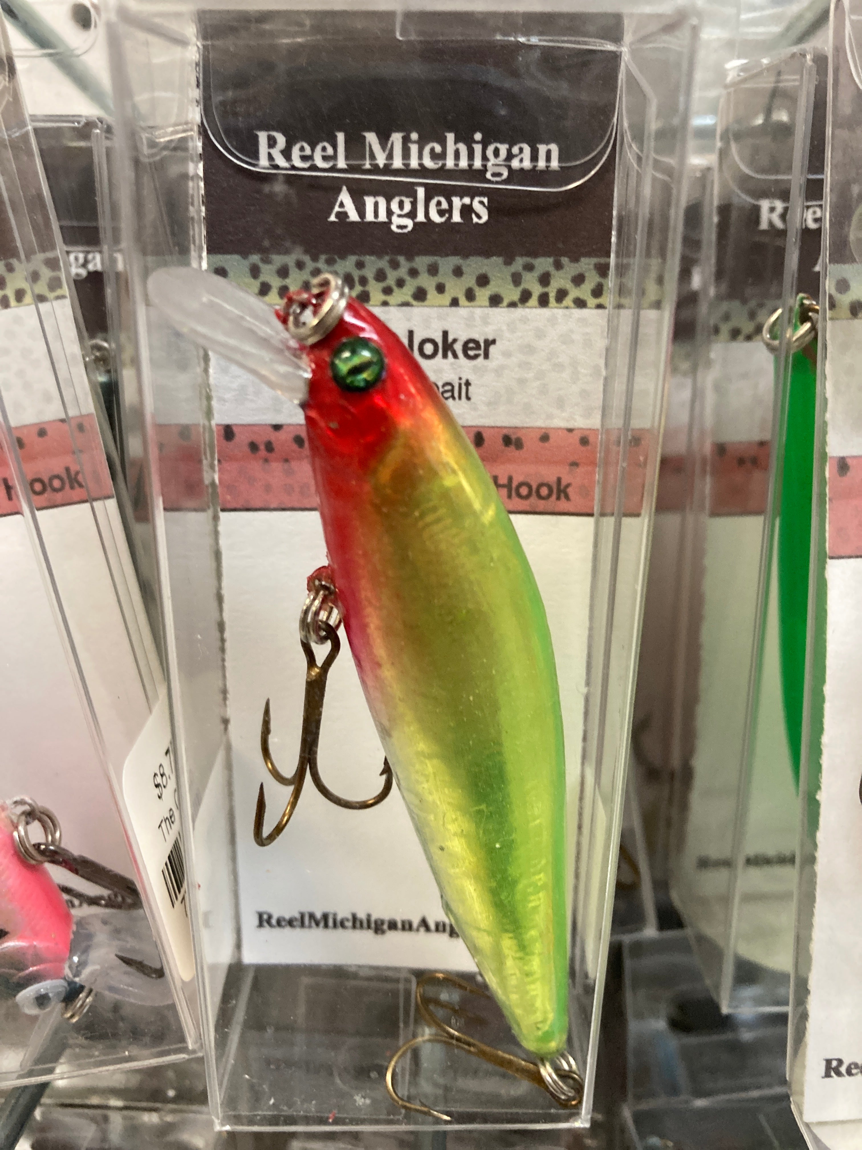 Fishing lure with green body, red head, and darker eye detail; treble hook