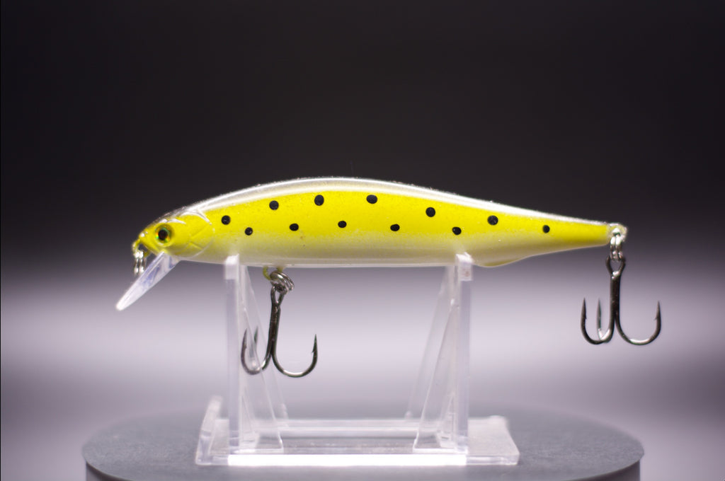 Yellow floating minnow-style jerkbait with black spots and treble hooks on clear stand