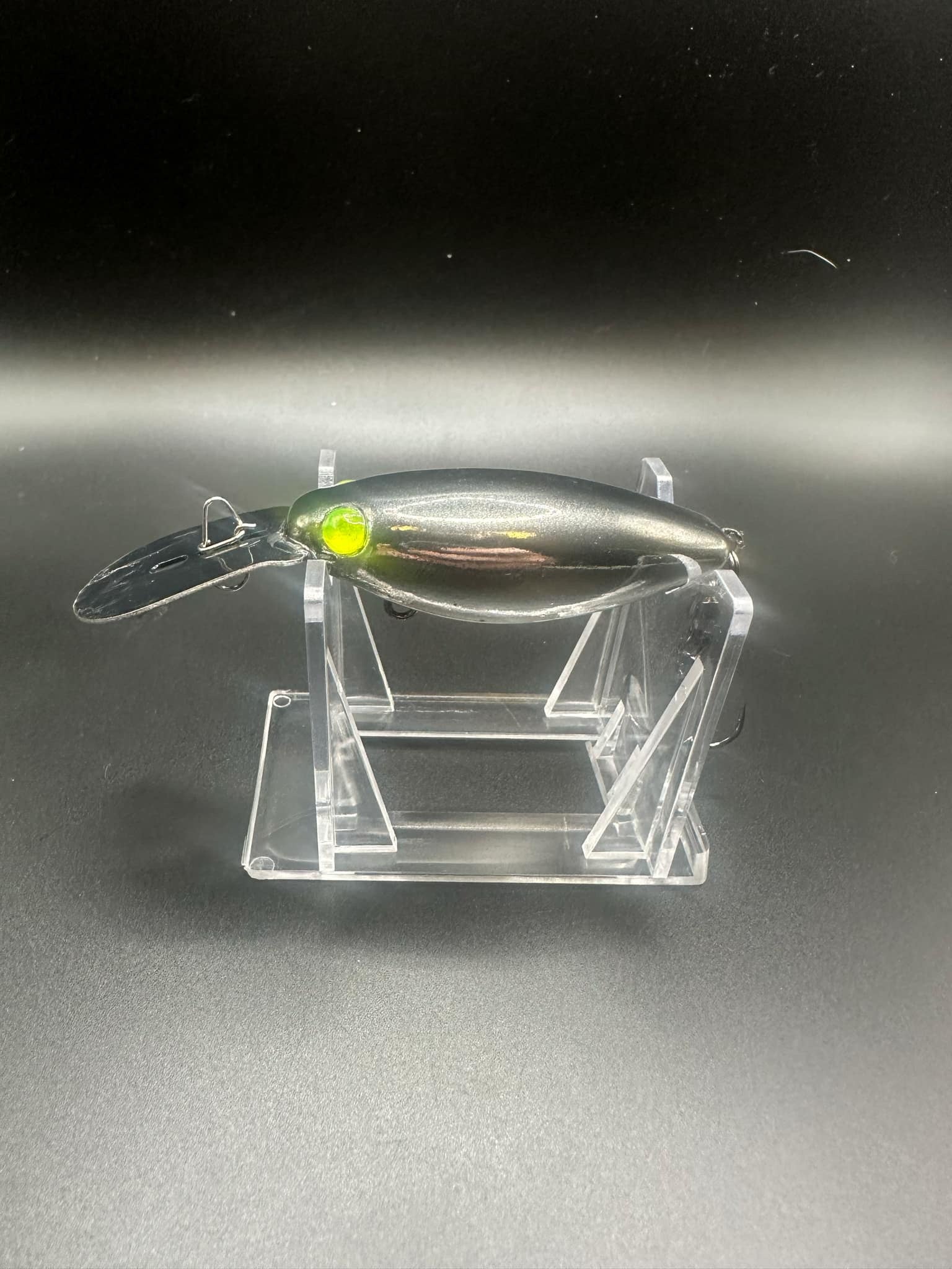Black Ops Chrome UV trolling plug with glowing green eye, side view on clear stand