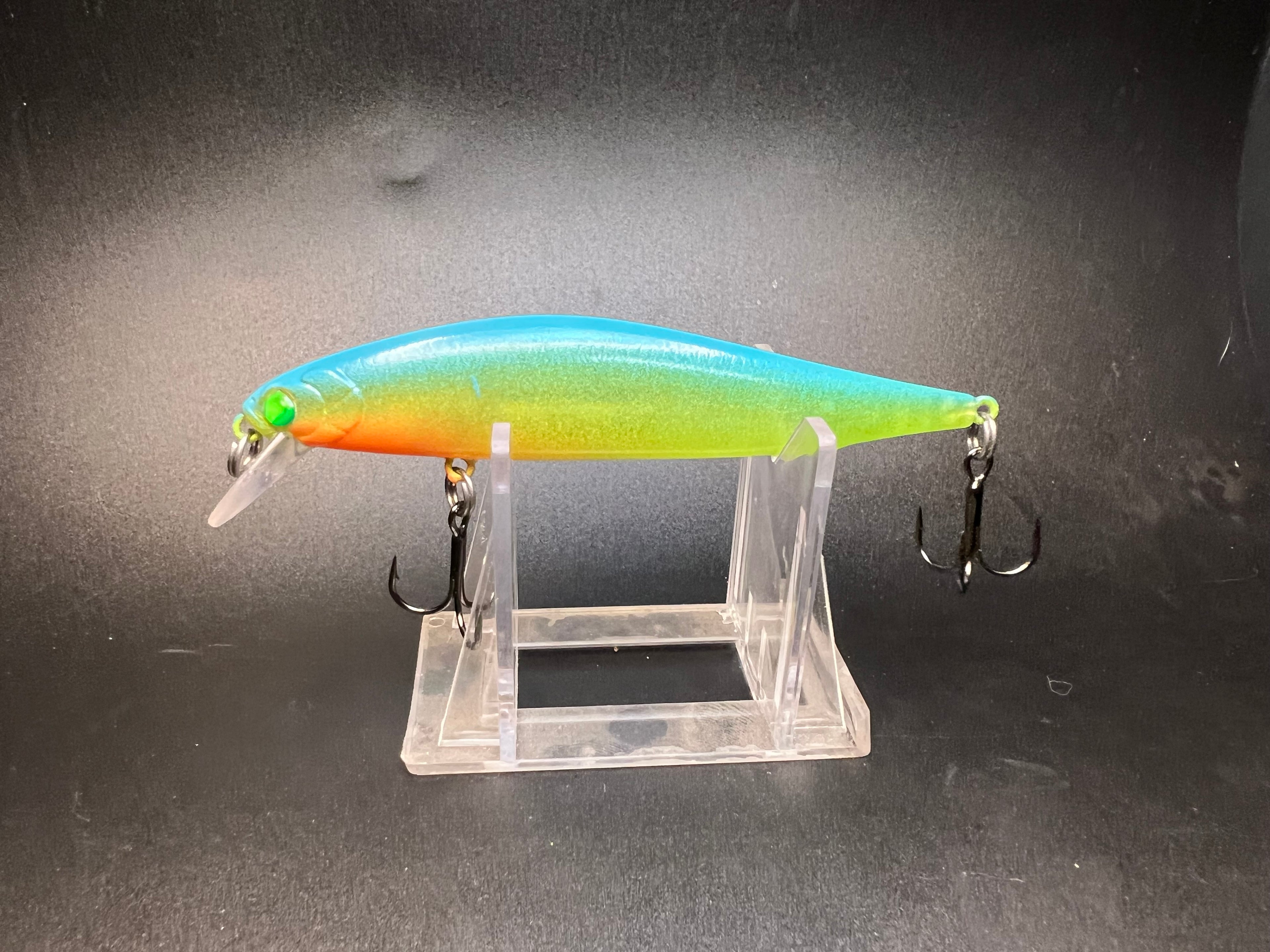 UV jerkbait lure with blue-green top and orange belly, clear body and treble hooks.