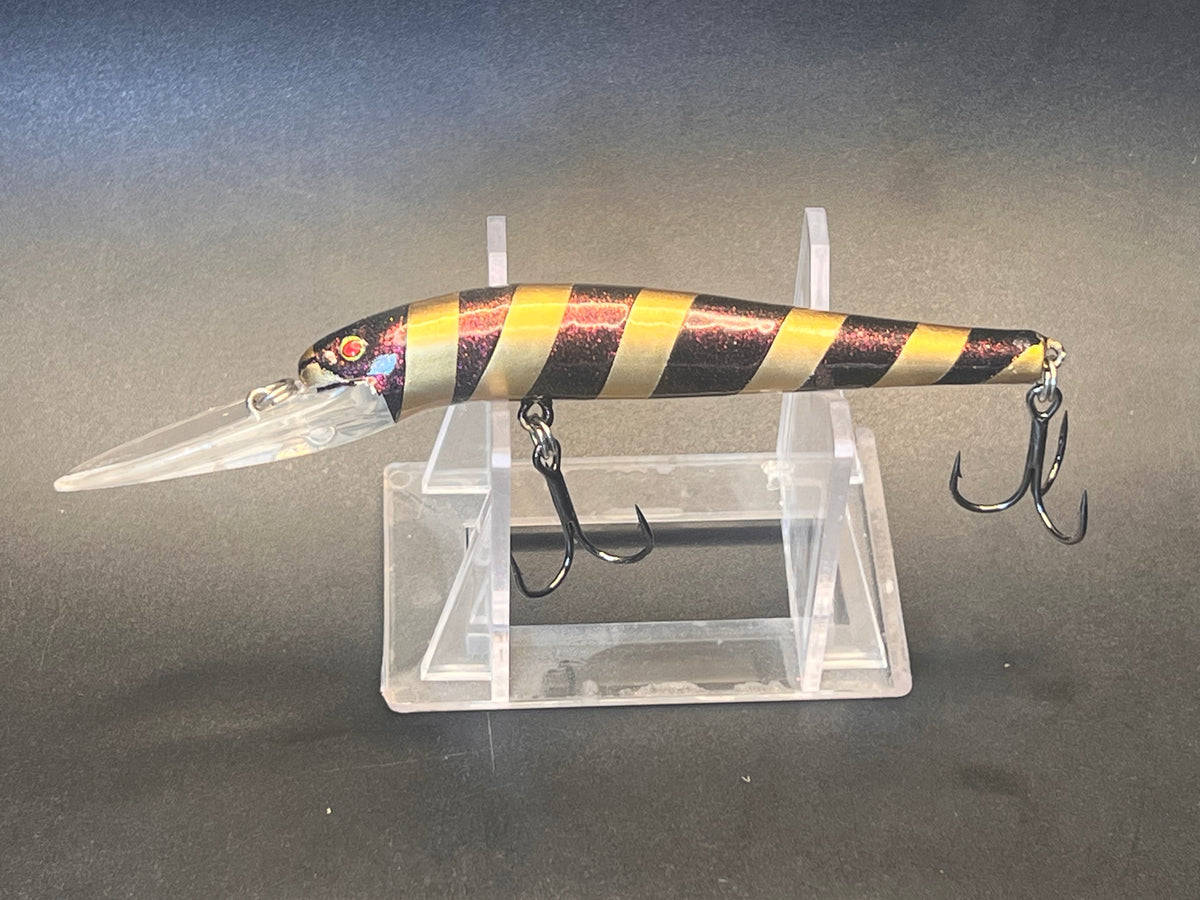 Striped fishing lure with two metal treble hooks, on clear display stand.