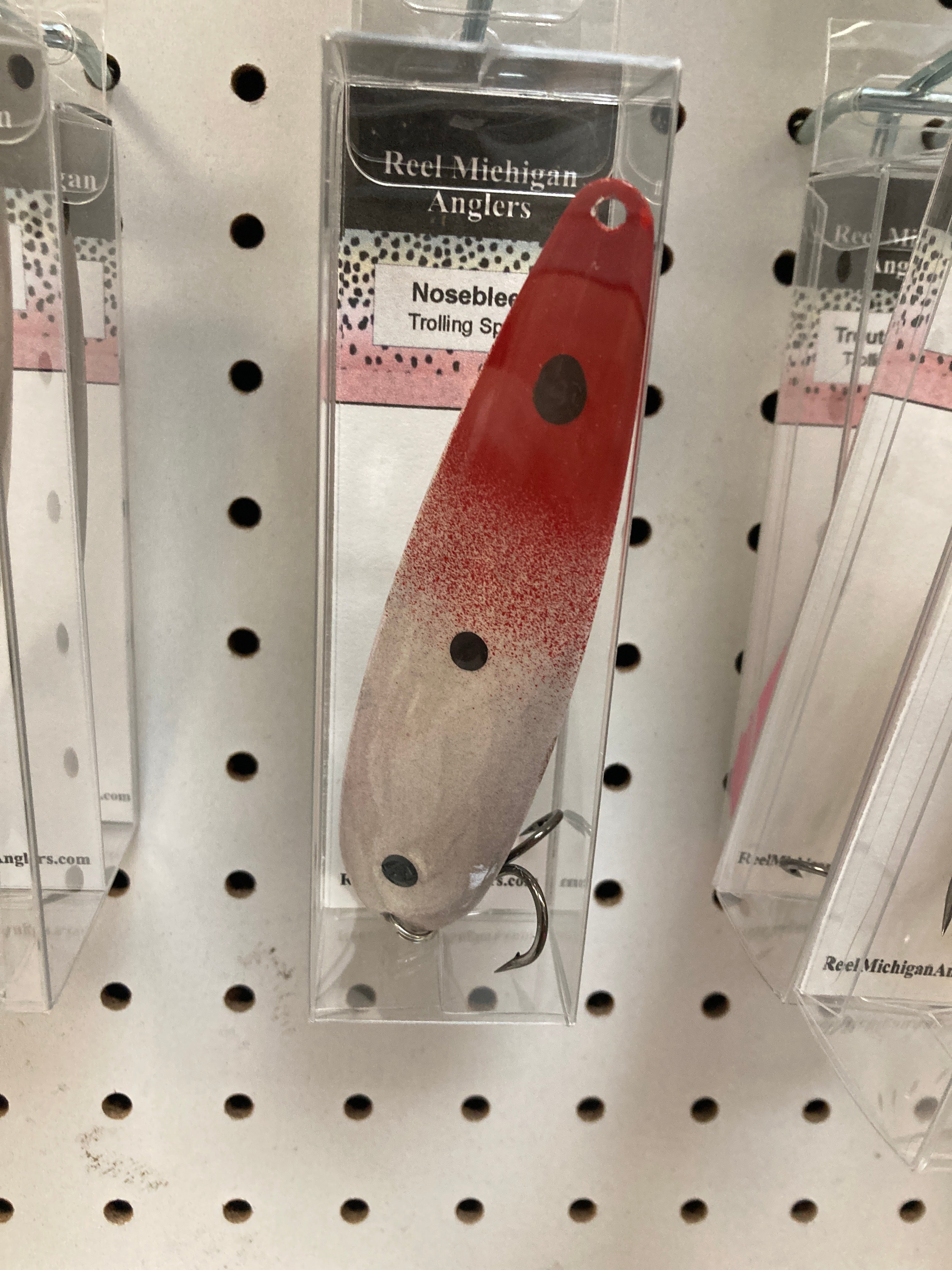 Red and silver trolling spoon with dark round spots, in retail blister pack