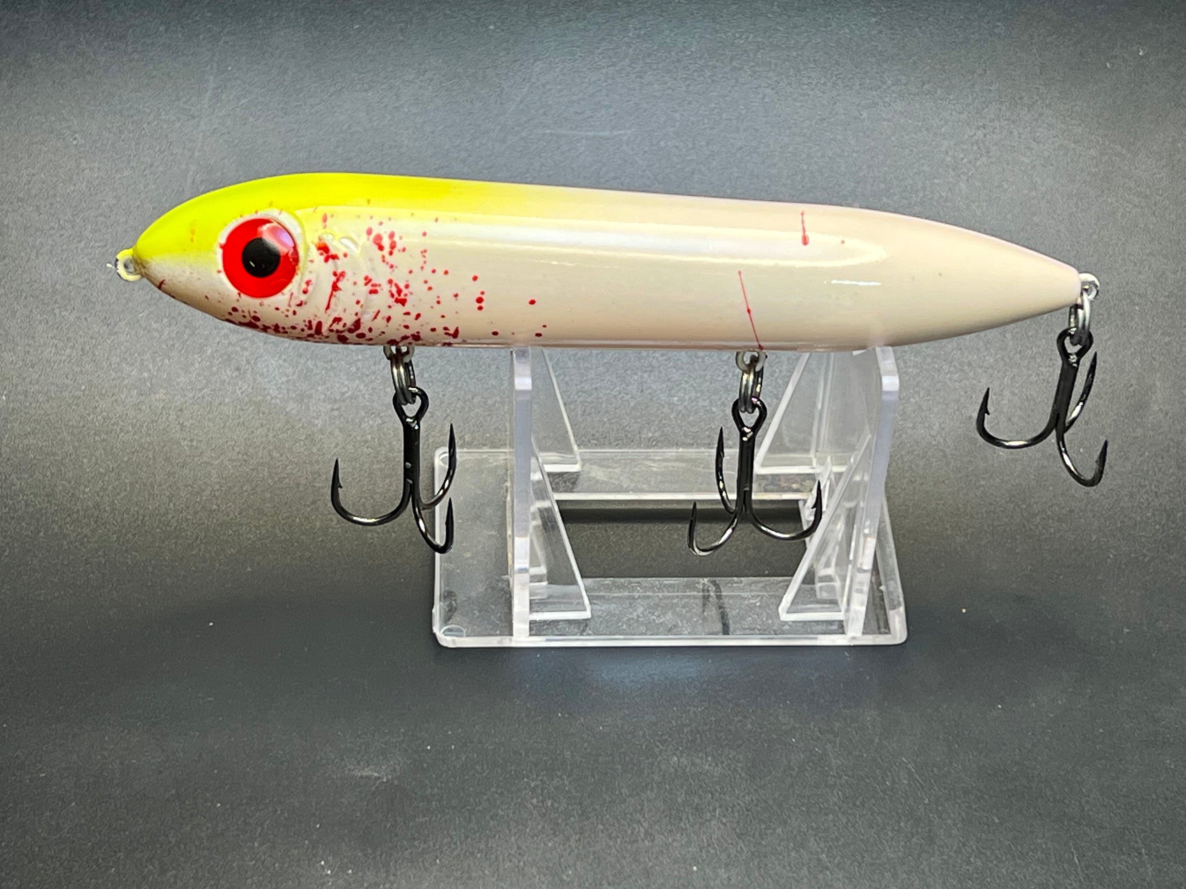 Topwater fishing lure with pale yellow body, red eye, and treble hooks