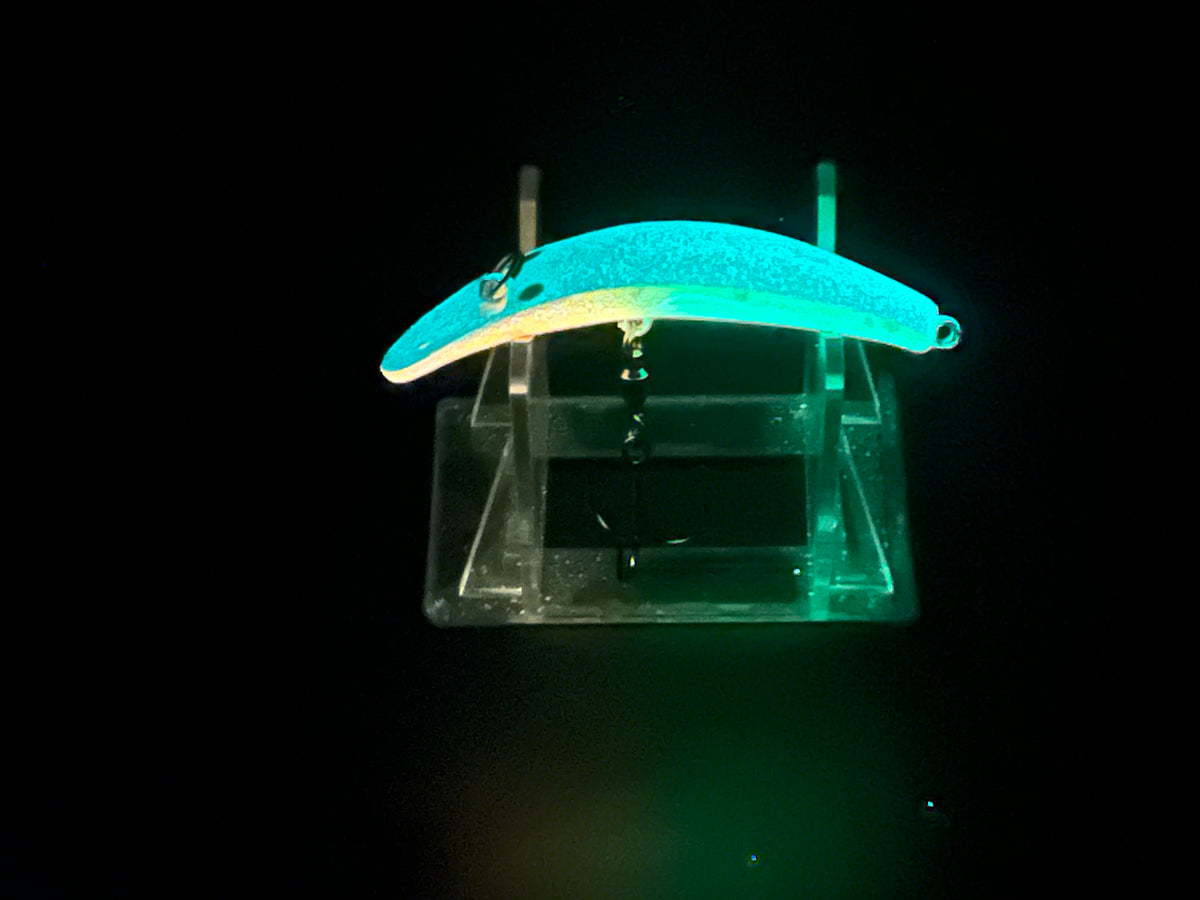 Glow fishing lure with teal body and dorsal fin, on clear acrylic display stand