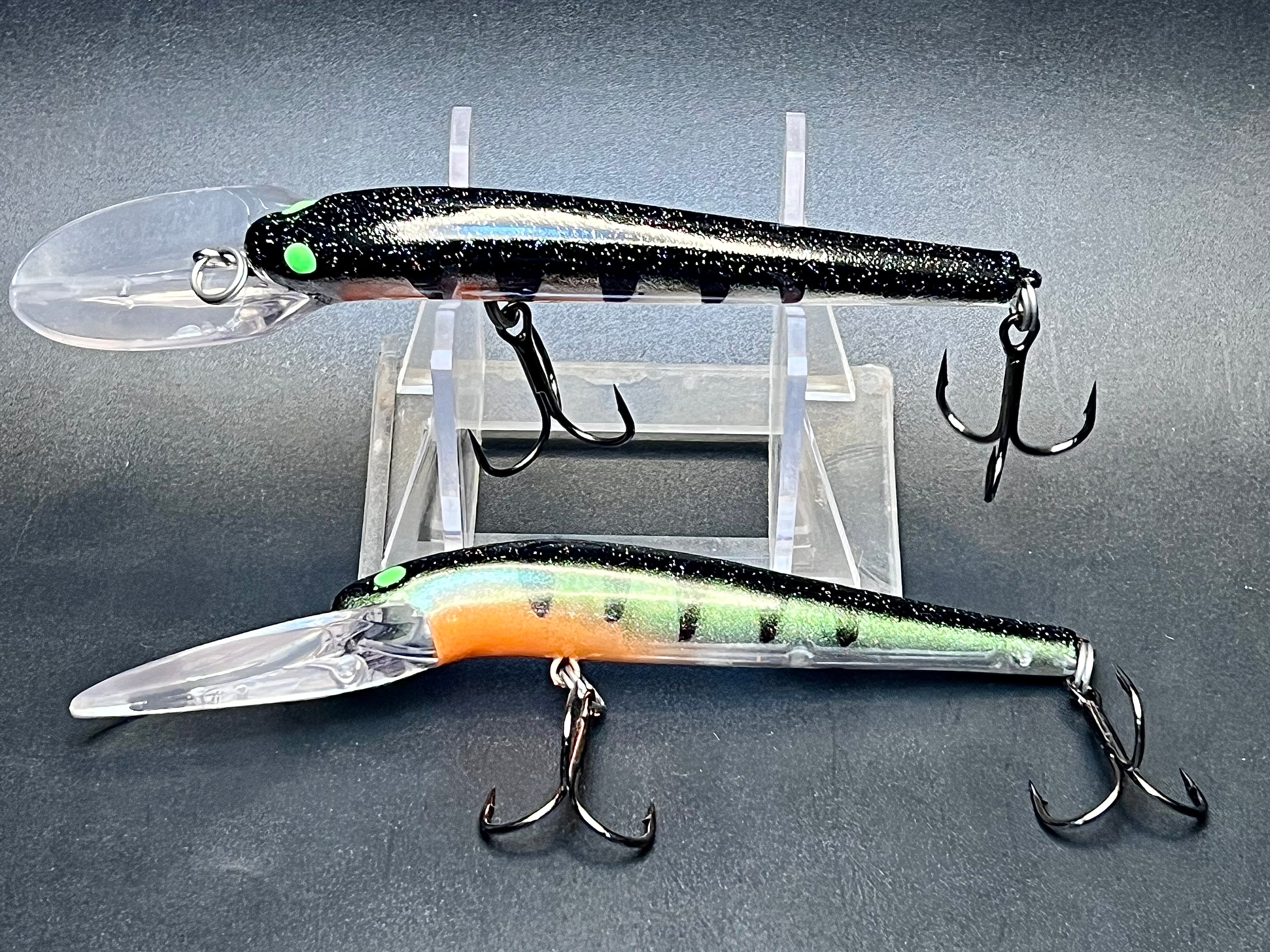 Fishing lure with black body and green accents, paired with orange lure on stand
