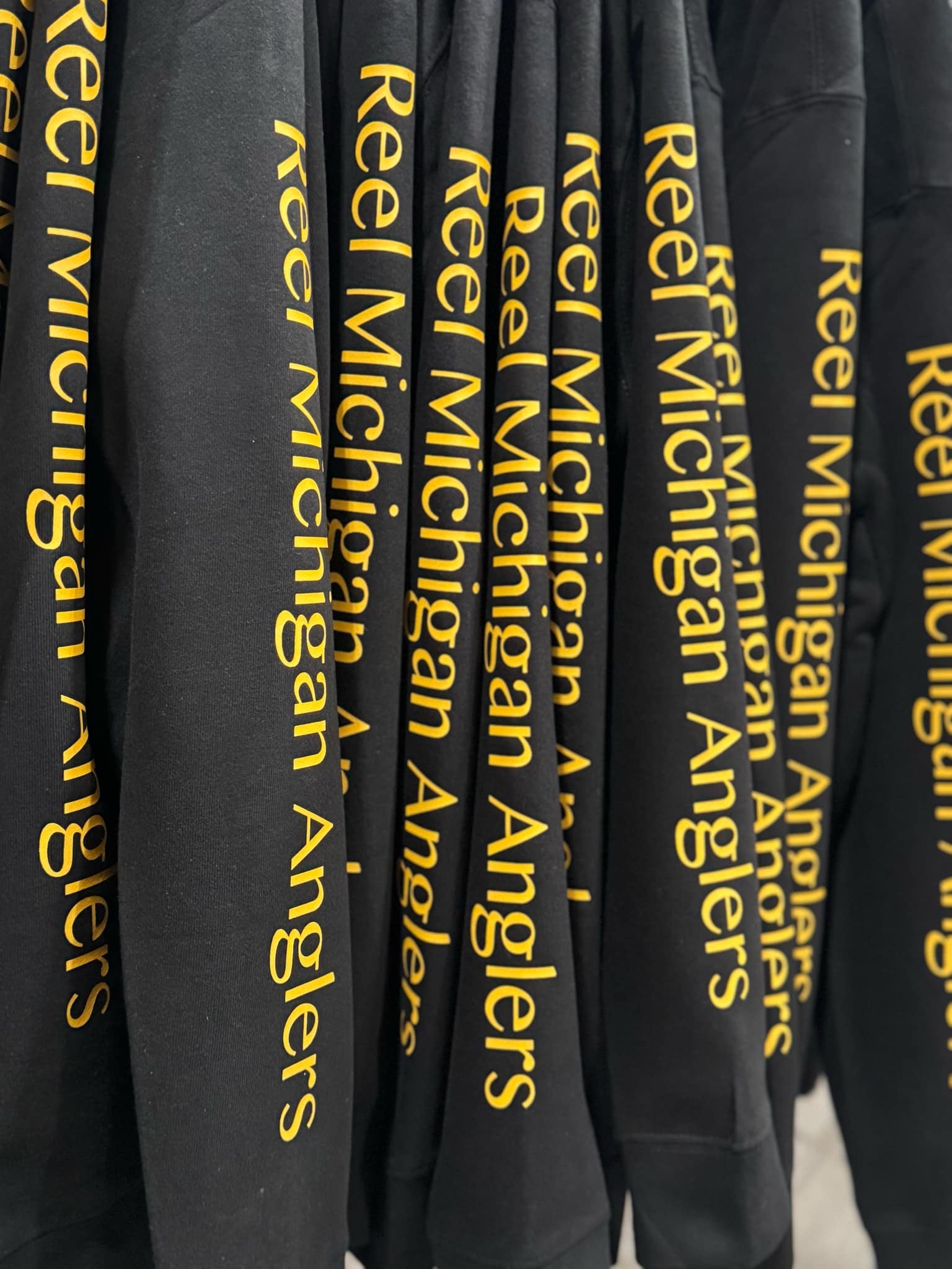 Charcoal hoodies with repeating yellow 'Reel Michigan Anglers' text on sleeves