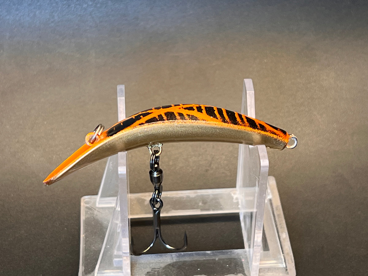 Black-and-orange striped fishing lure with curved body and exposed treble hook