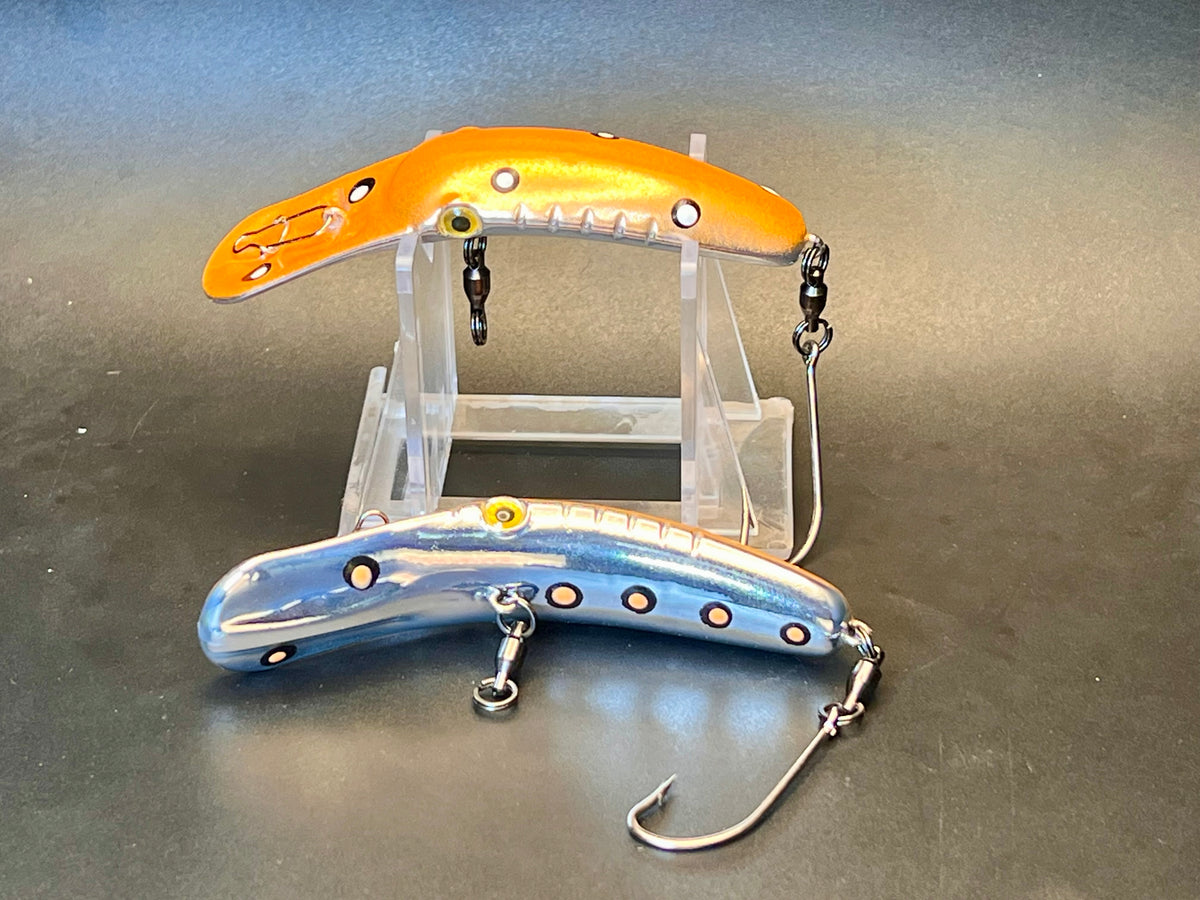 Two fishing plug lures on clear stand: orange and blue bodies with metal hooks