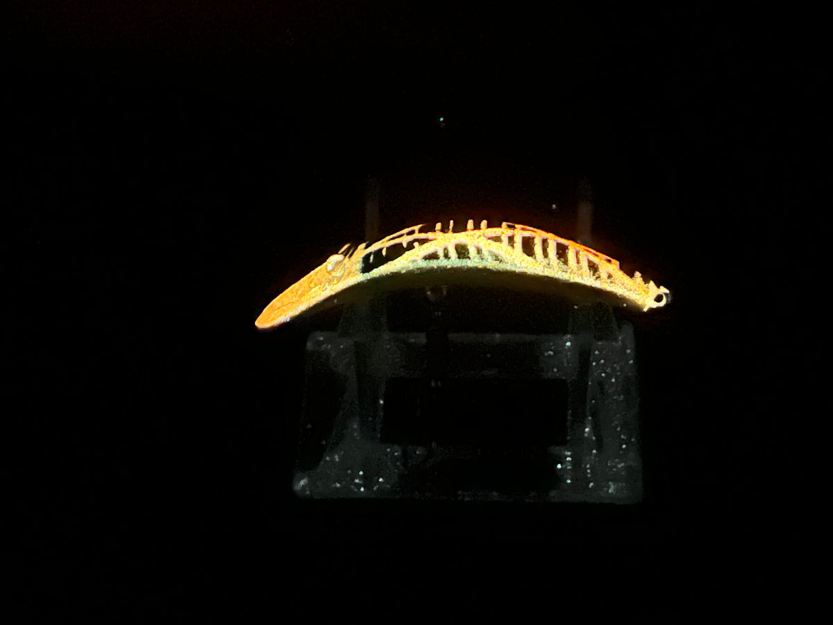 Yellow glowing fishing lure with curved profile, shown on dark stand