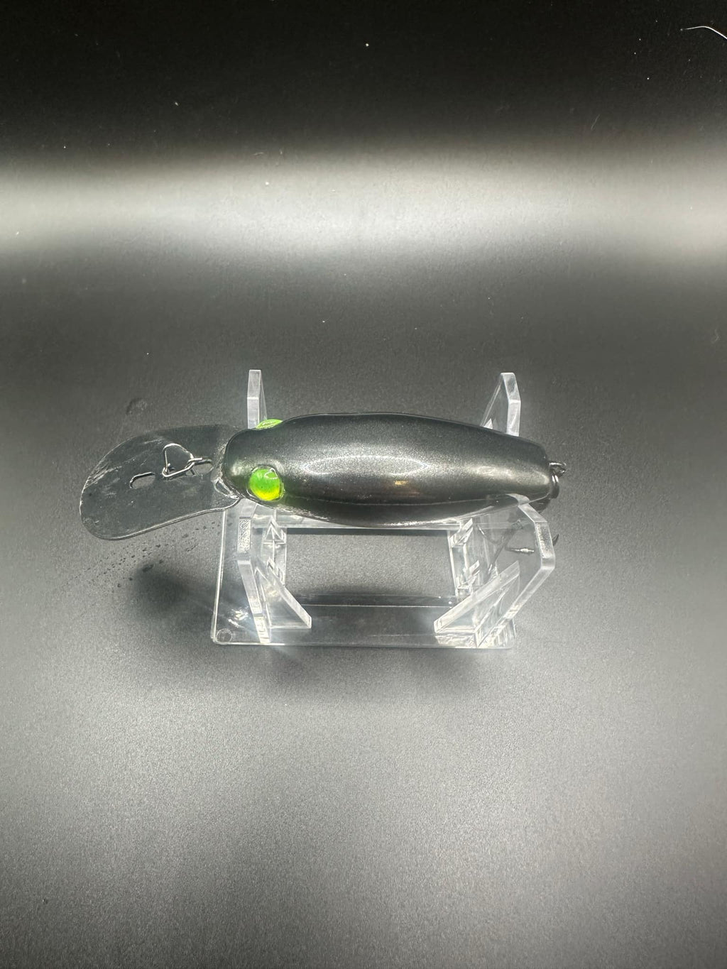 Chrome UV trolling plug, black body with green eye; top view on clear stand