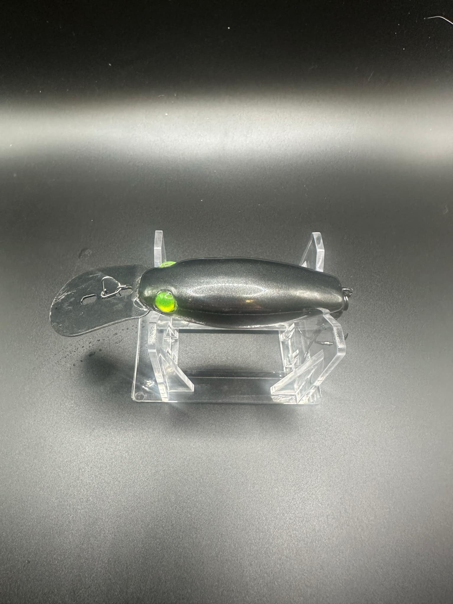 Chrome UV trolling plug, black body with green eye; top view on clear stand