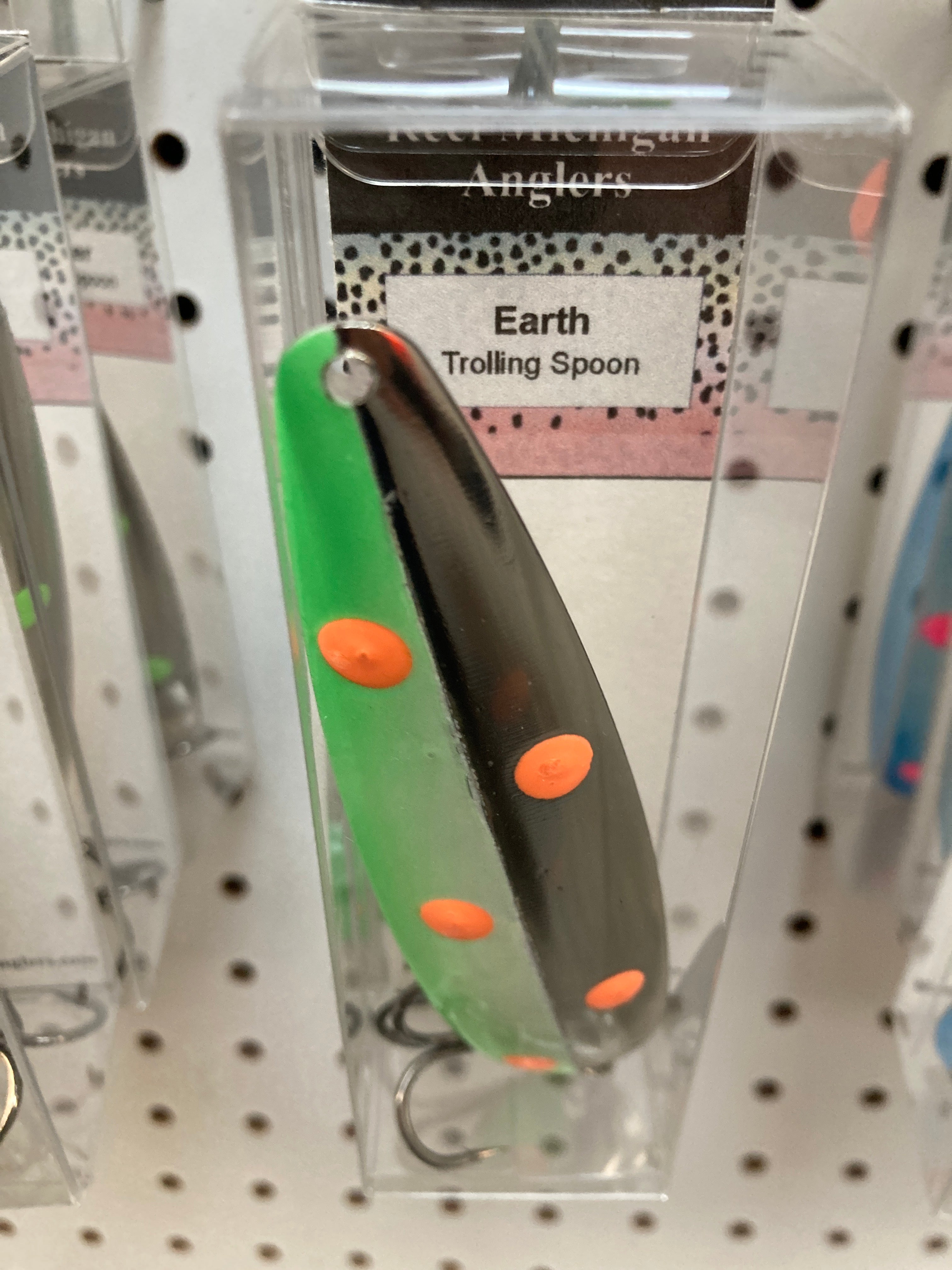 Green and gray trolling spoon with orange spot accents, in retail blister pack
