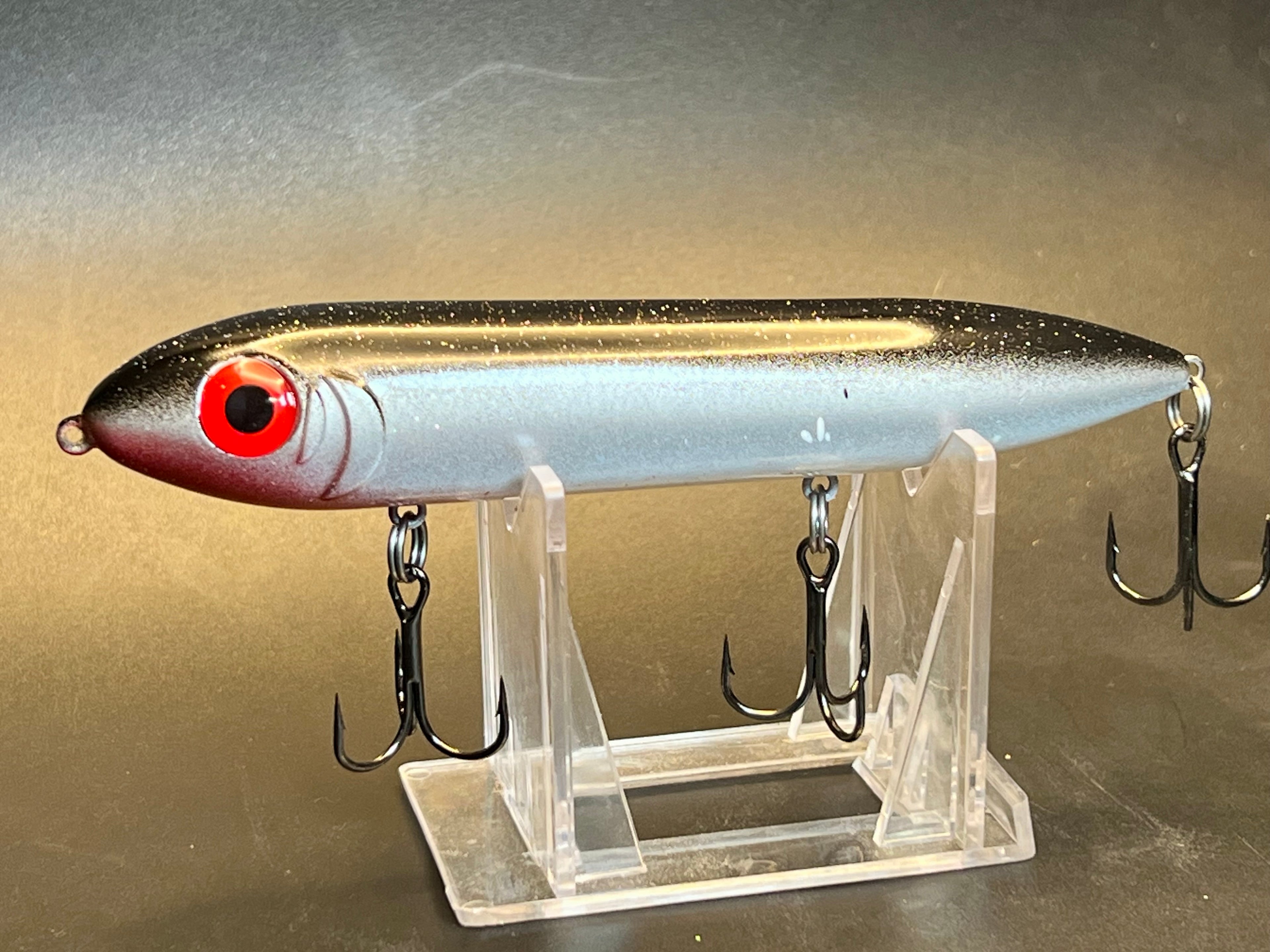 Silver topwater fishing lure with red head, metal body, two treble hooks