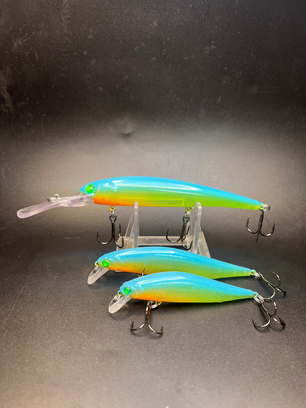 Two UV jerkbait lures with blue-green bodies and orange belly, clear plugs and treble hooks.