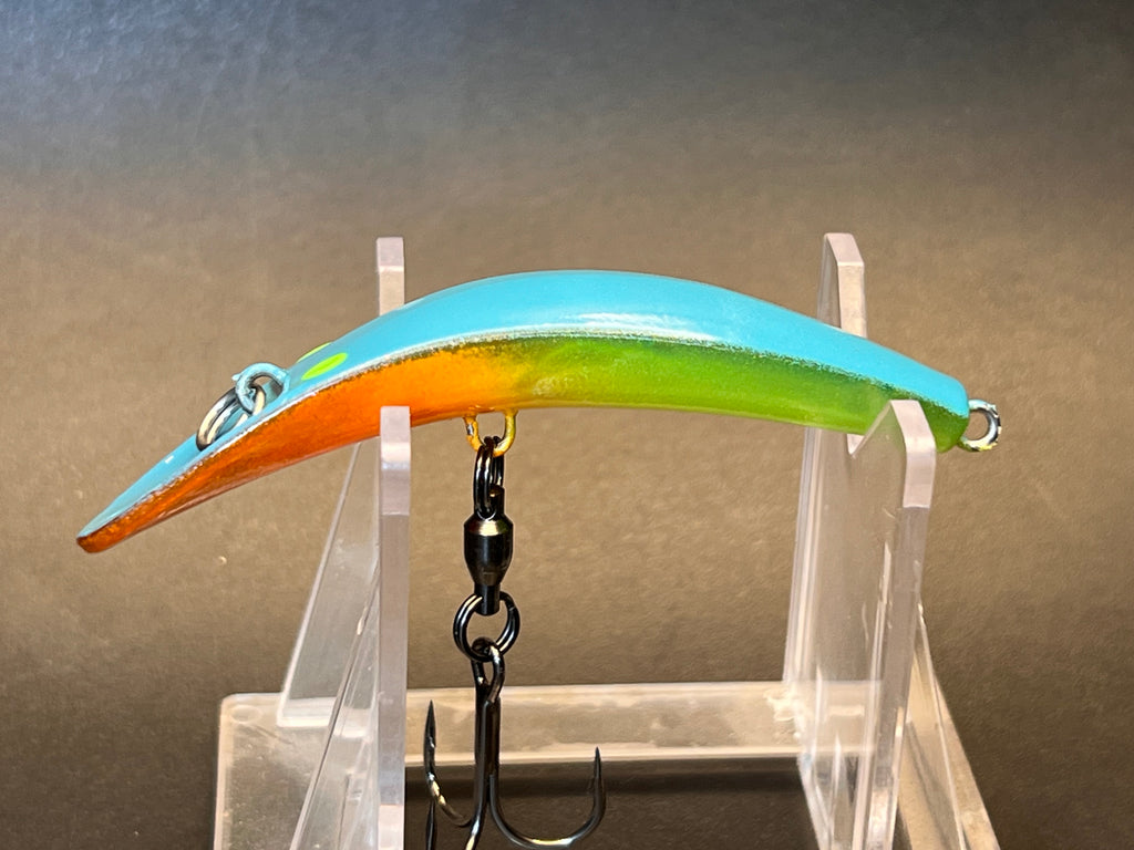 Fishing lure with orange and green striped body, blue top, on clear stand