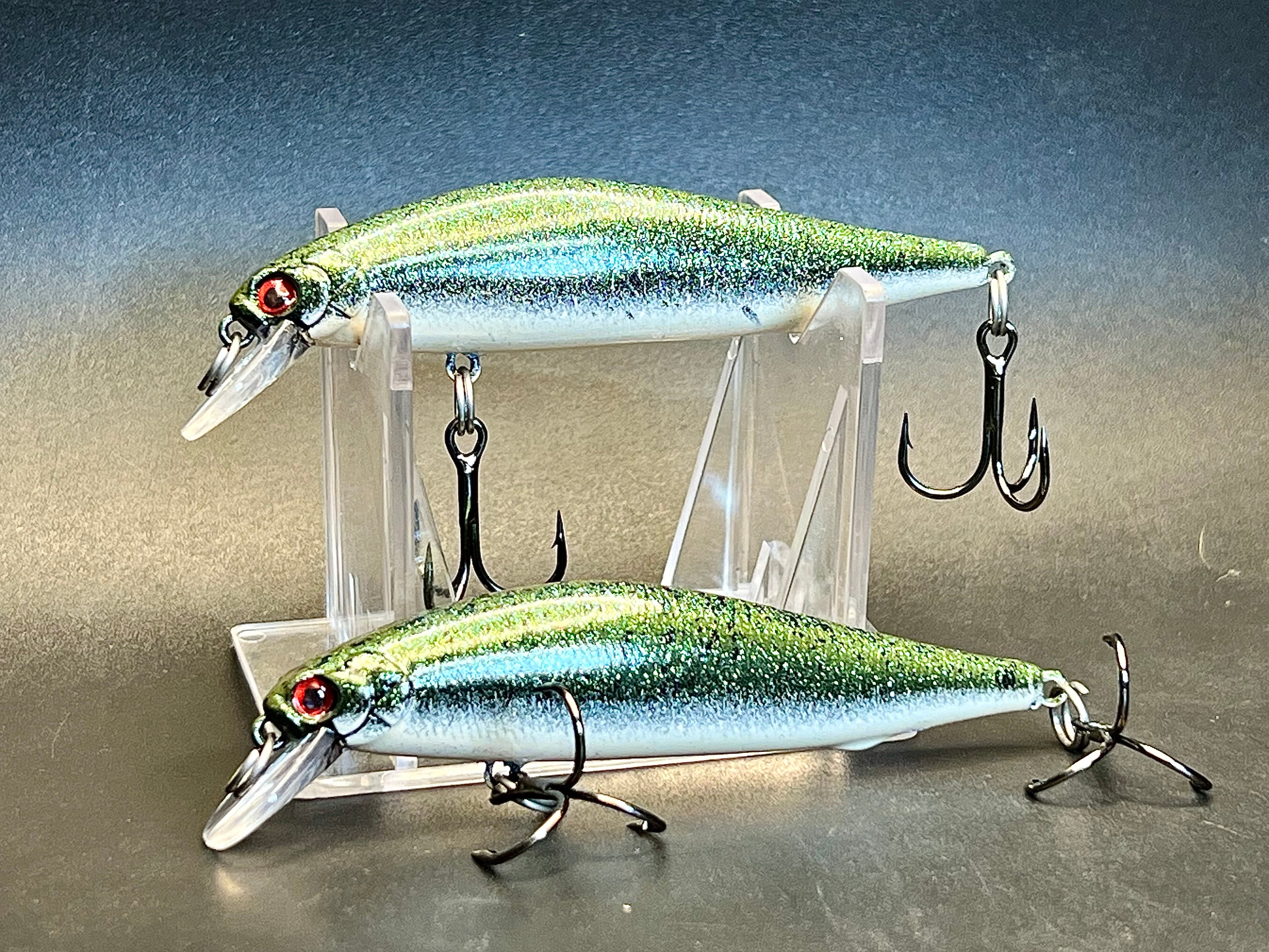 Two silver-blue jerkbait lures with green glitter stripes and treble hooks