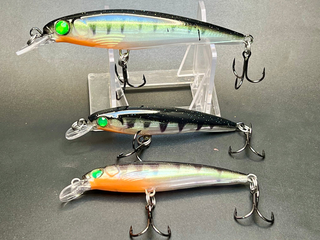Three fishing lures, clear body with orange and green accents, treble hooks