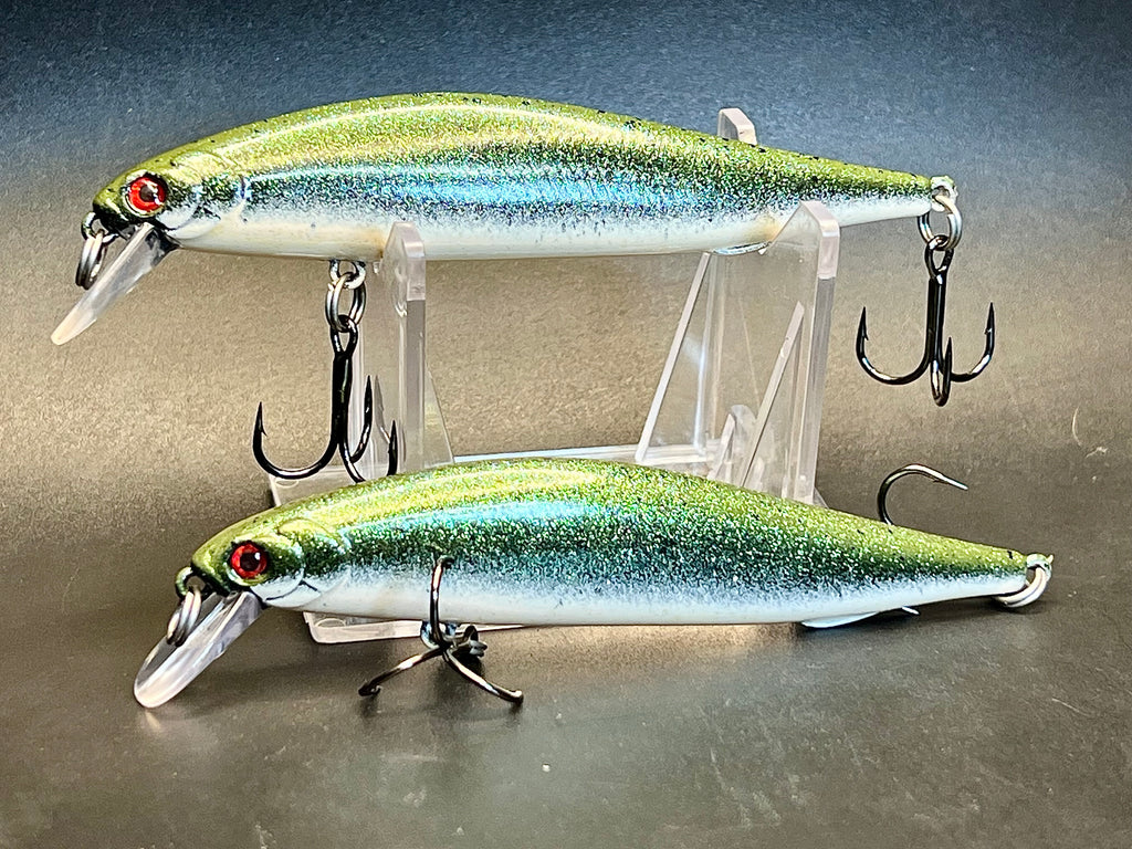 Two green-silver jerkbait lures with red eyes, clear lip, and treble hooks