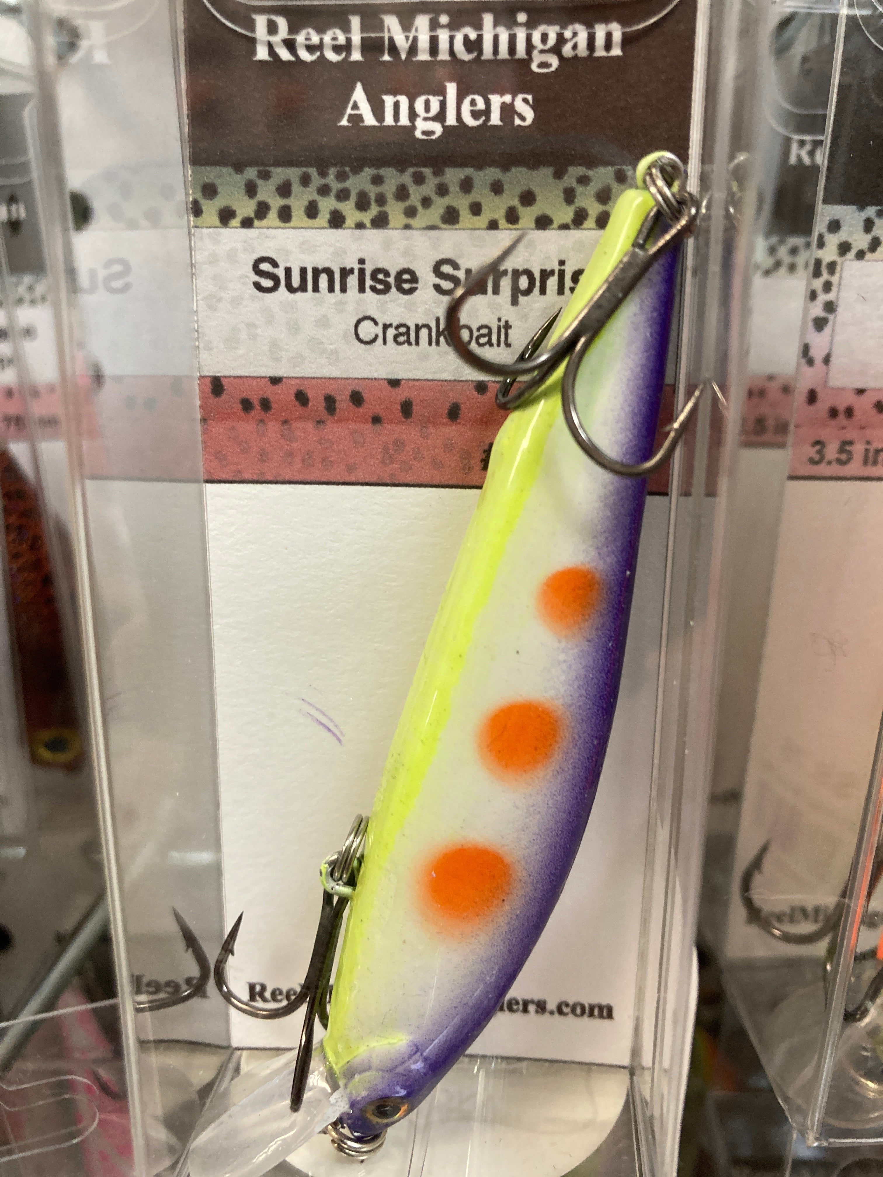 Fishing lure with purple-to-yellow sunrise finish, orange spots, and treble hook