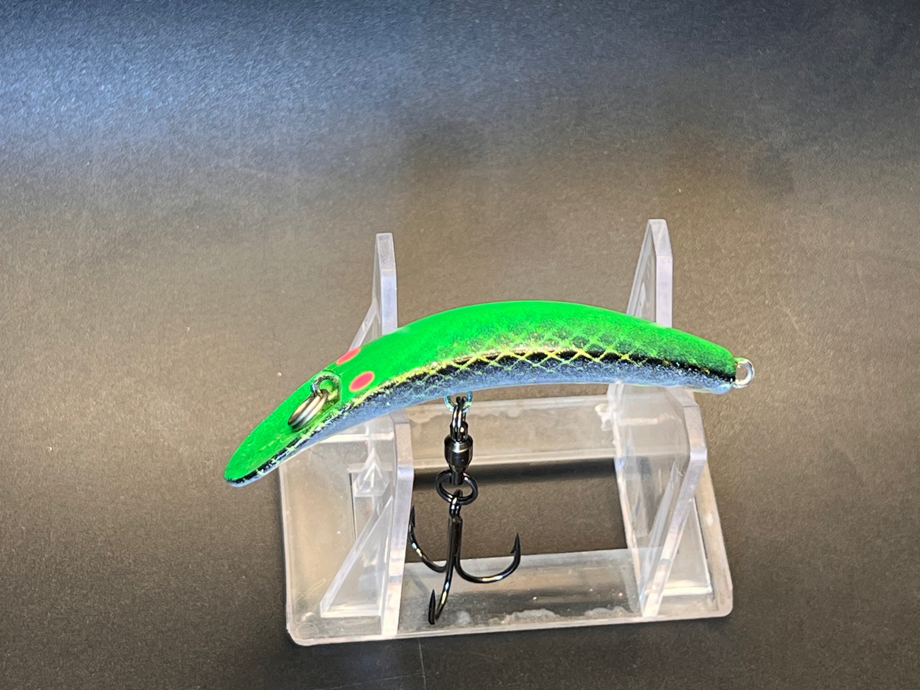 Green fish-shaped fishing lure with blue underside and two treble hooks on stand