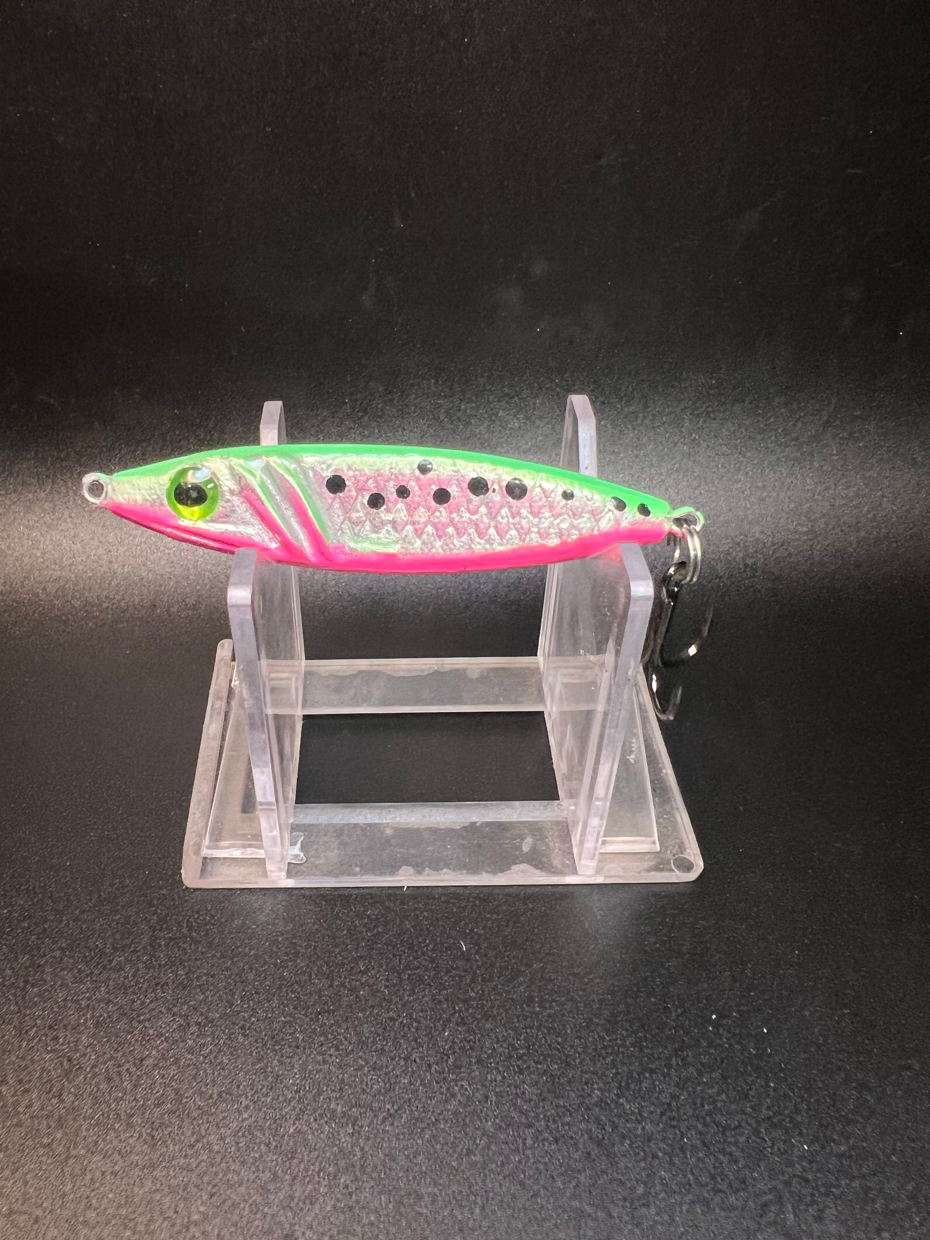 Jigging spoon lure: pink with green top, silver hook and treble on stand.