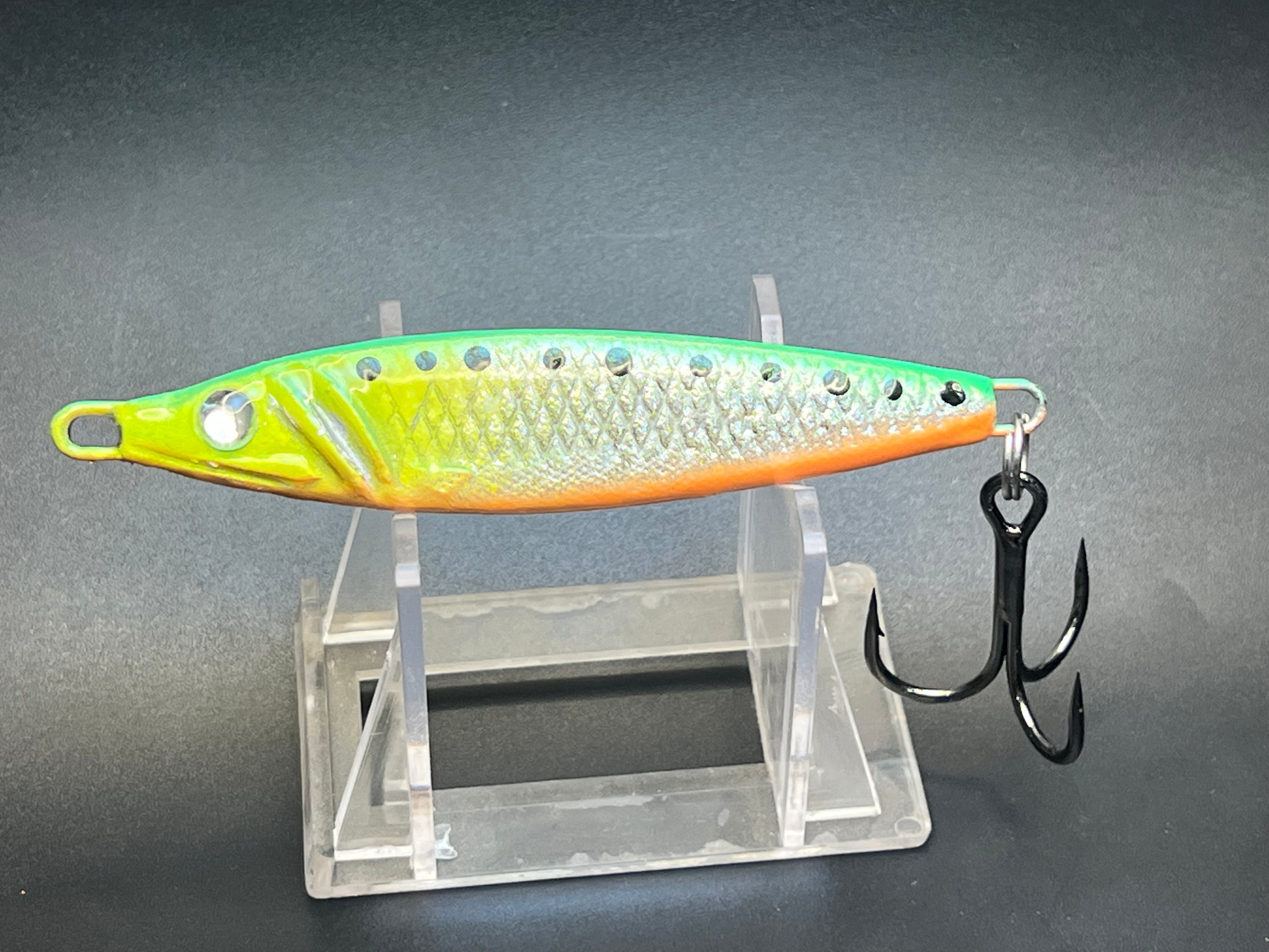 Fishing jigging spoon lure, yellow-lime and silver scales with orange belly, treble hook.