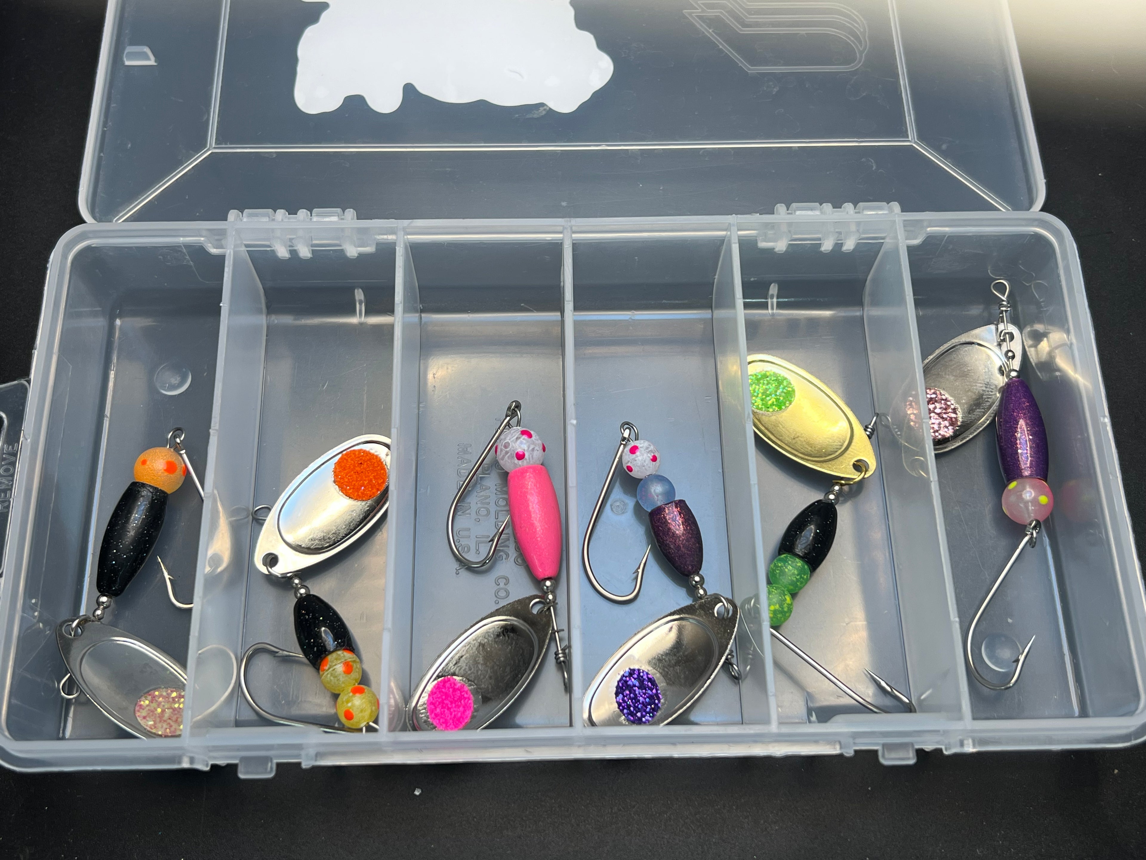 Clear tackle box with assorted colorful fishing spinner lures and hooks