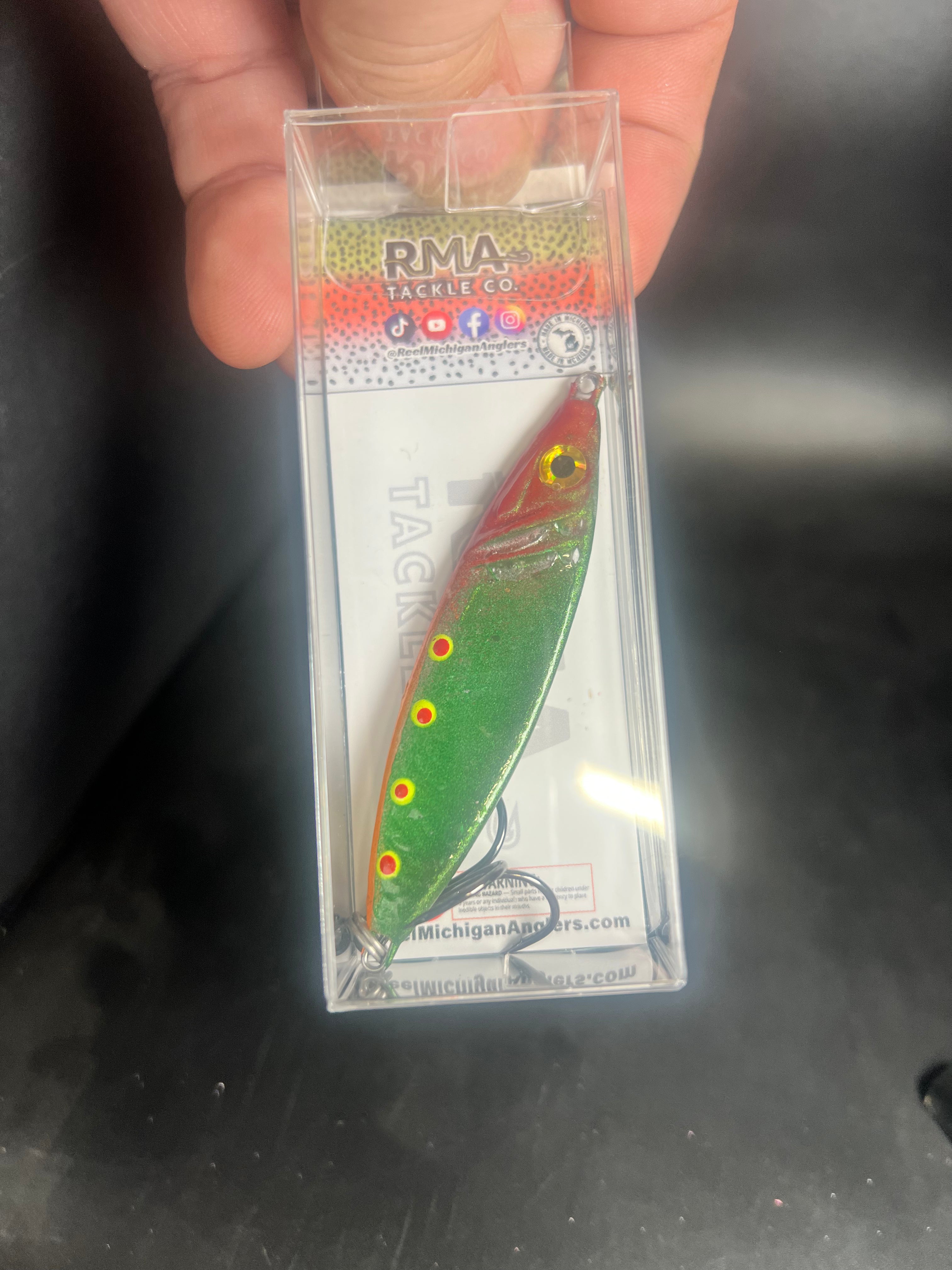 Salmon jigging spoon lure in clear blister pack, green body with orange accents and dots