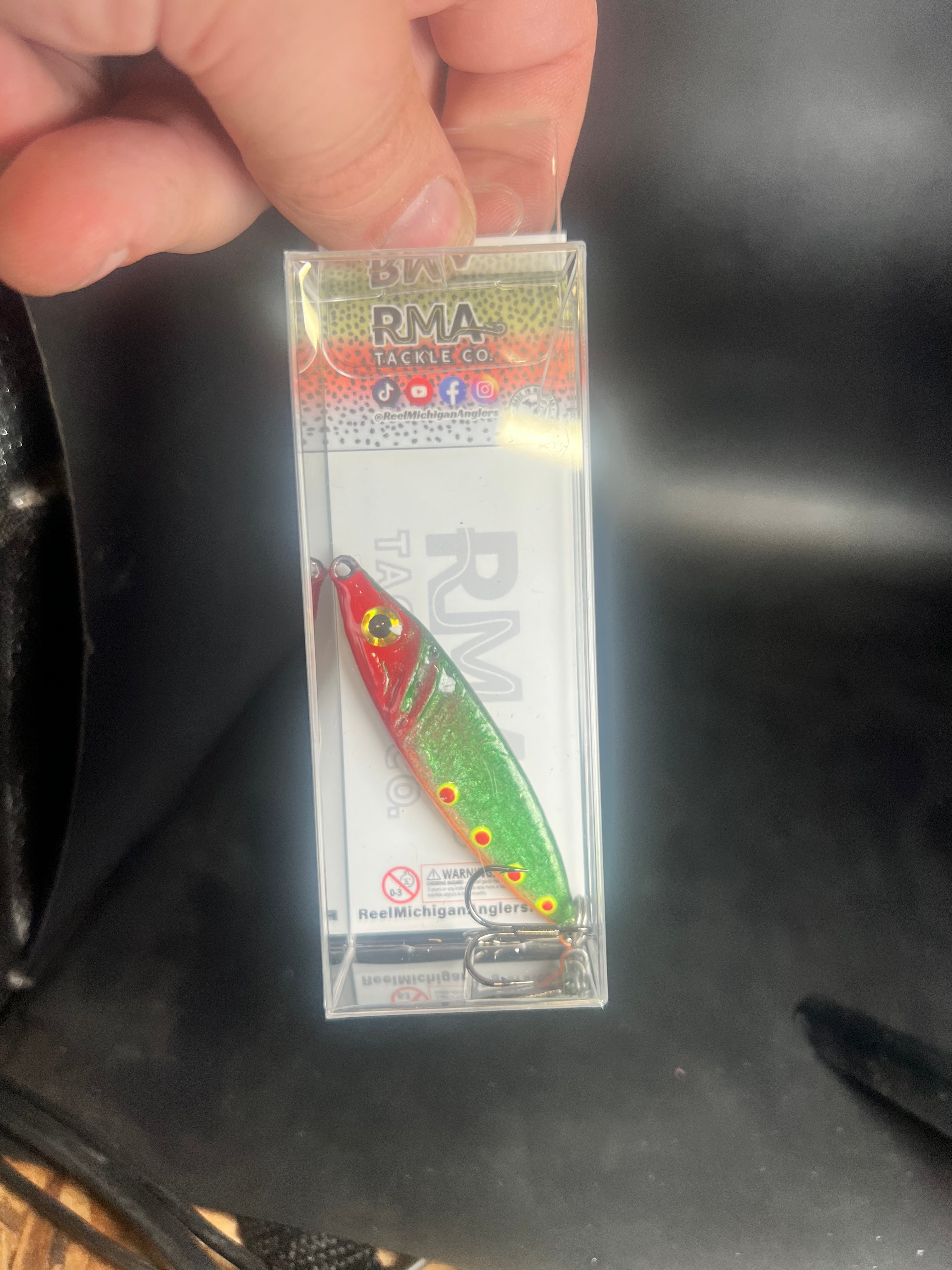 UV glow jigging spoon lure in clear blister pack, green red patterned body with hooks