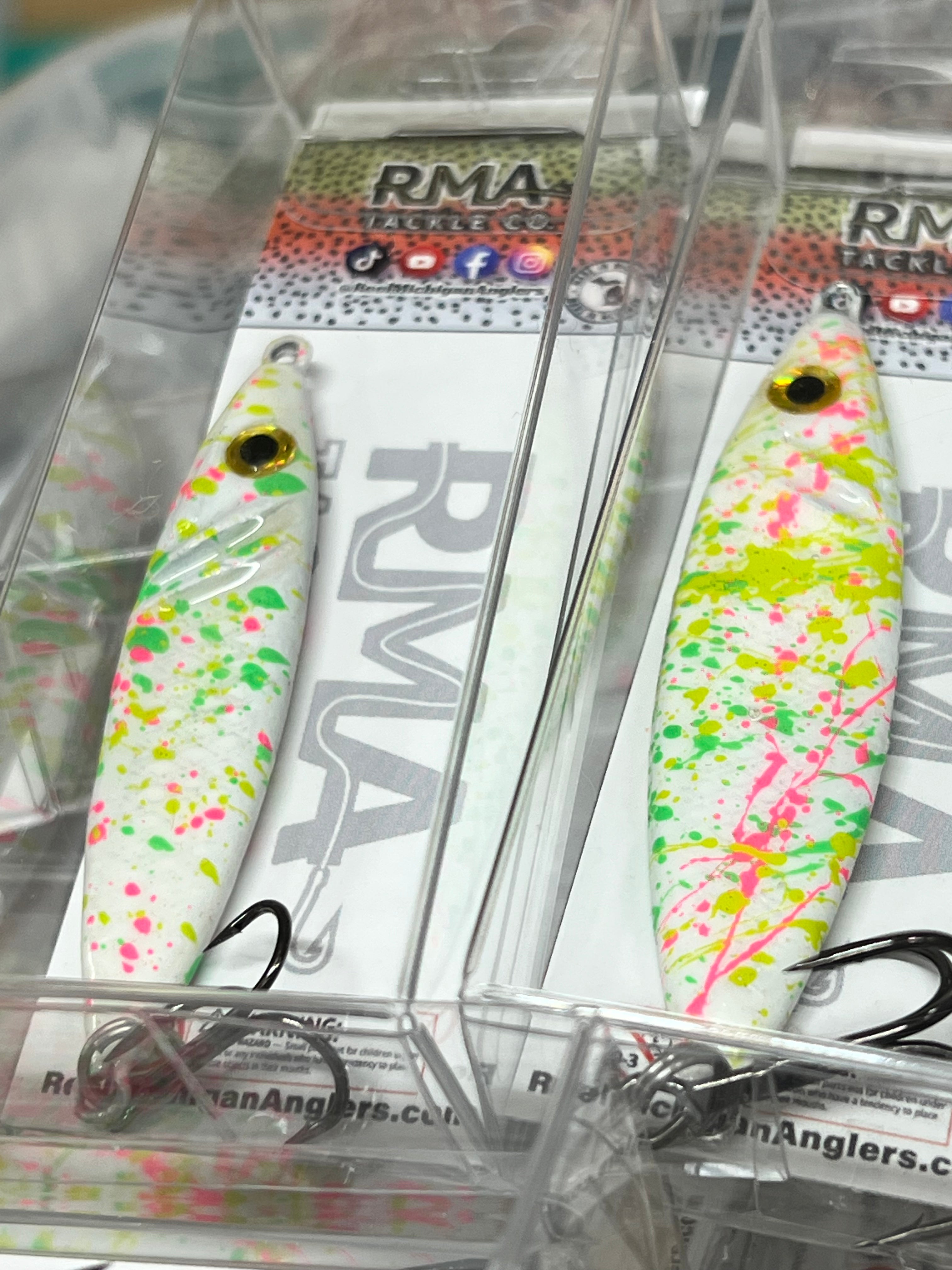 Pair of white jigging spoons with neon green and pink speckles, yellow eyes