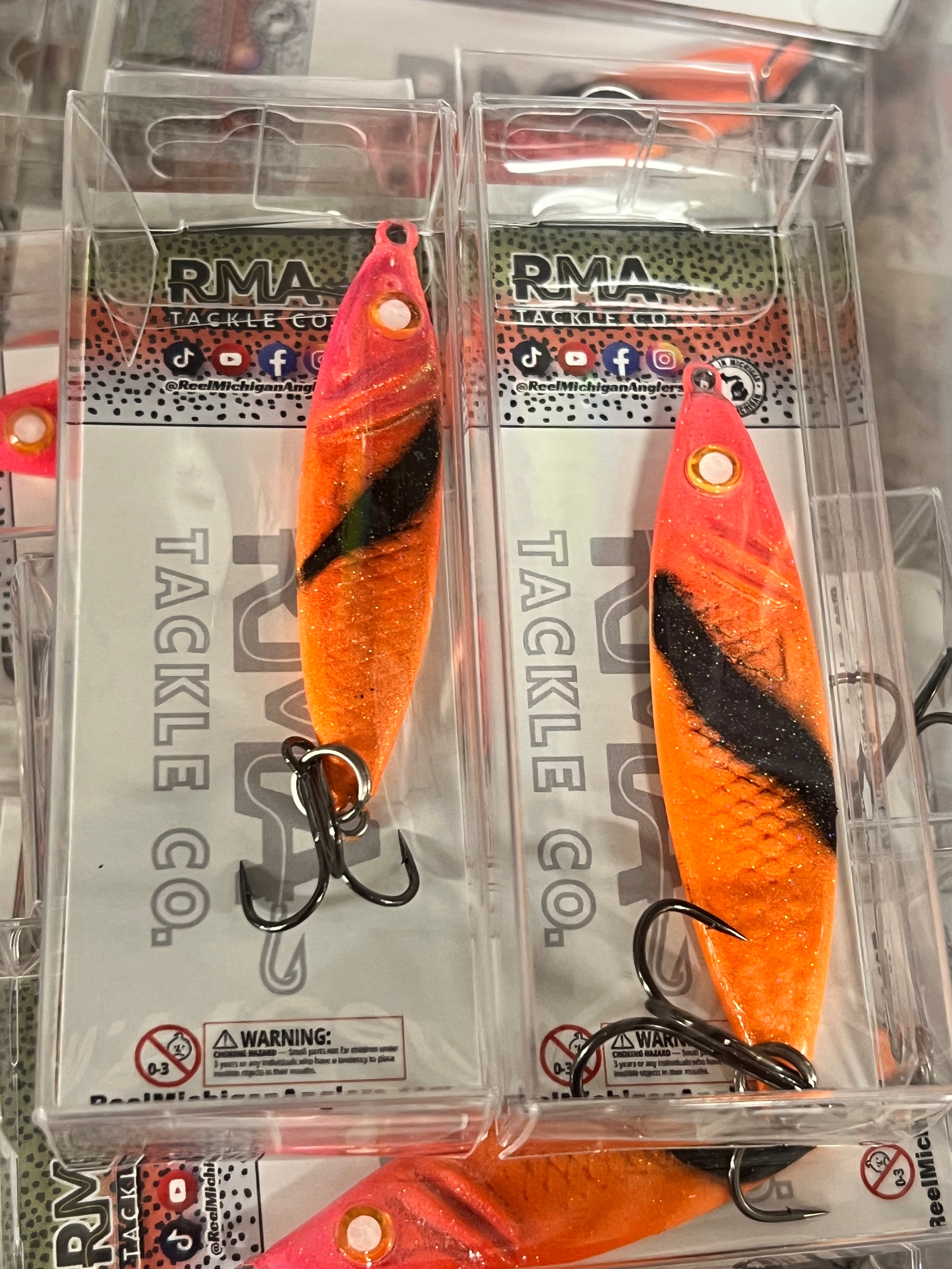 Orange jigging spoon with black side stripe, in clear blister packaging.