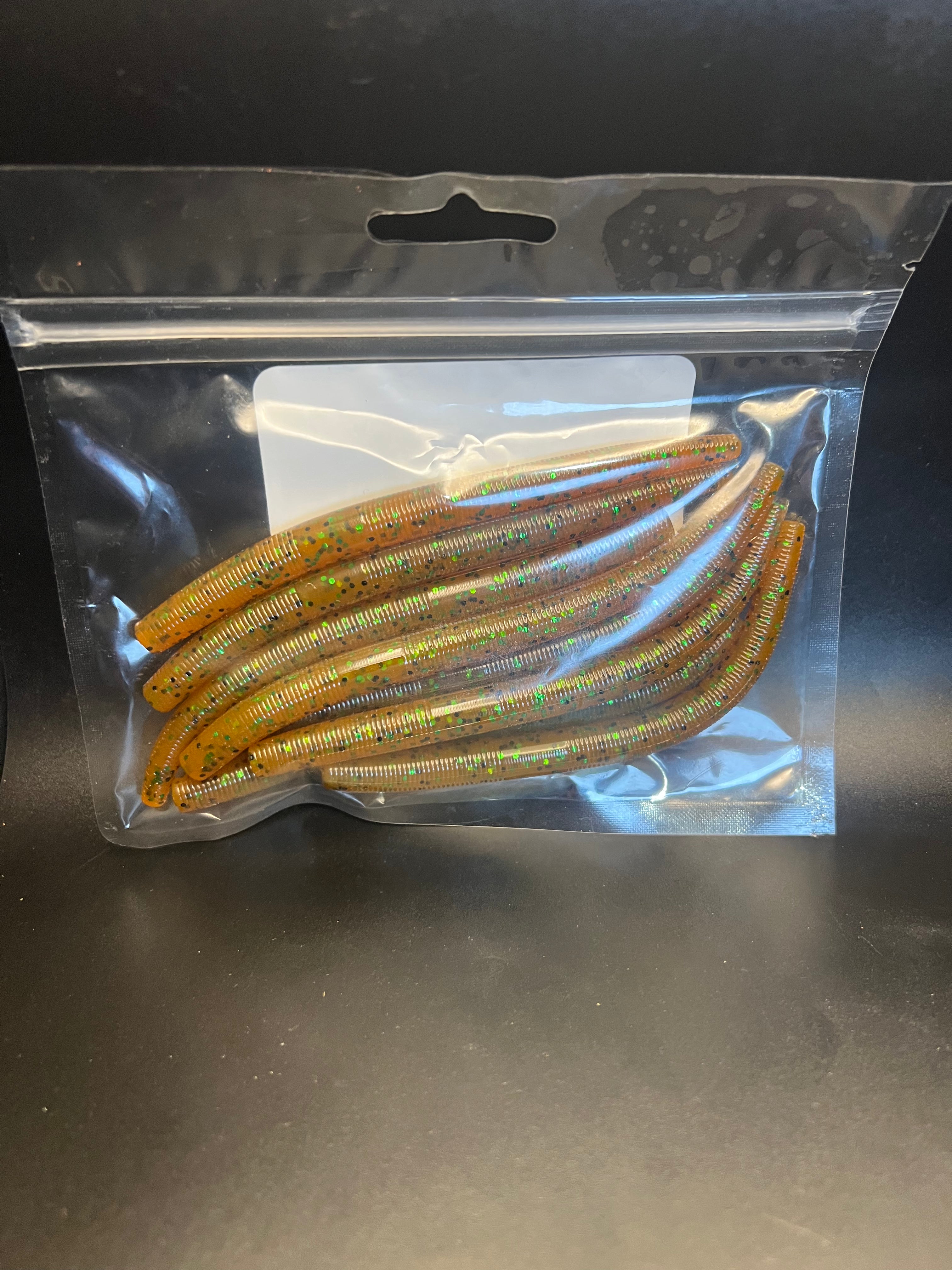 Soft plastic stickbait worms in golden-brown with green and red flecks inside clear pack