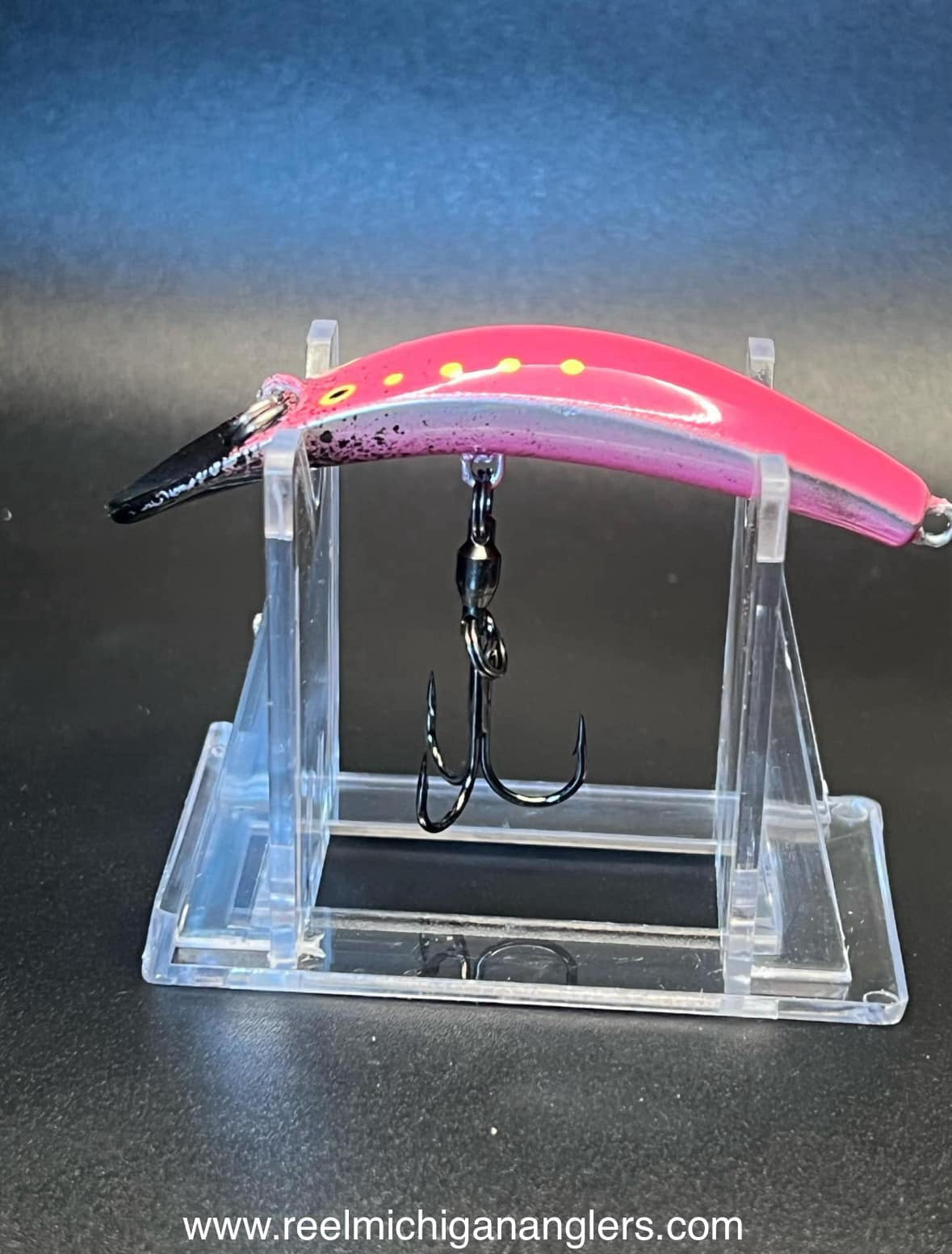 Pink lure with yellow dot band, black head, and treble hooks hanging from metal chain