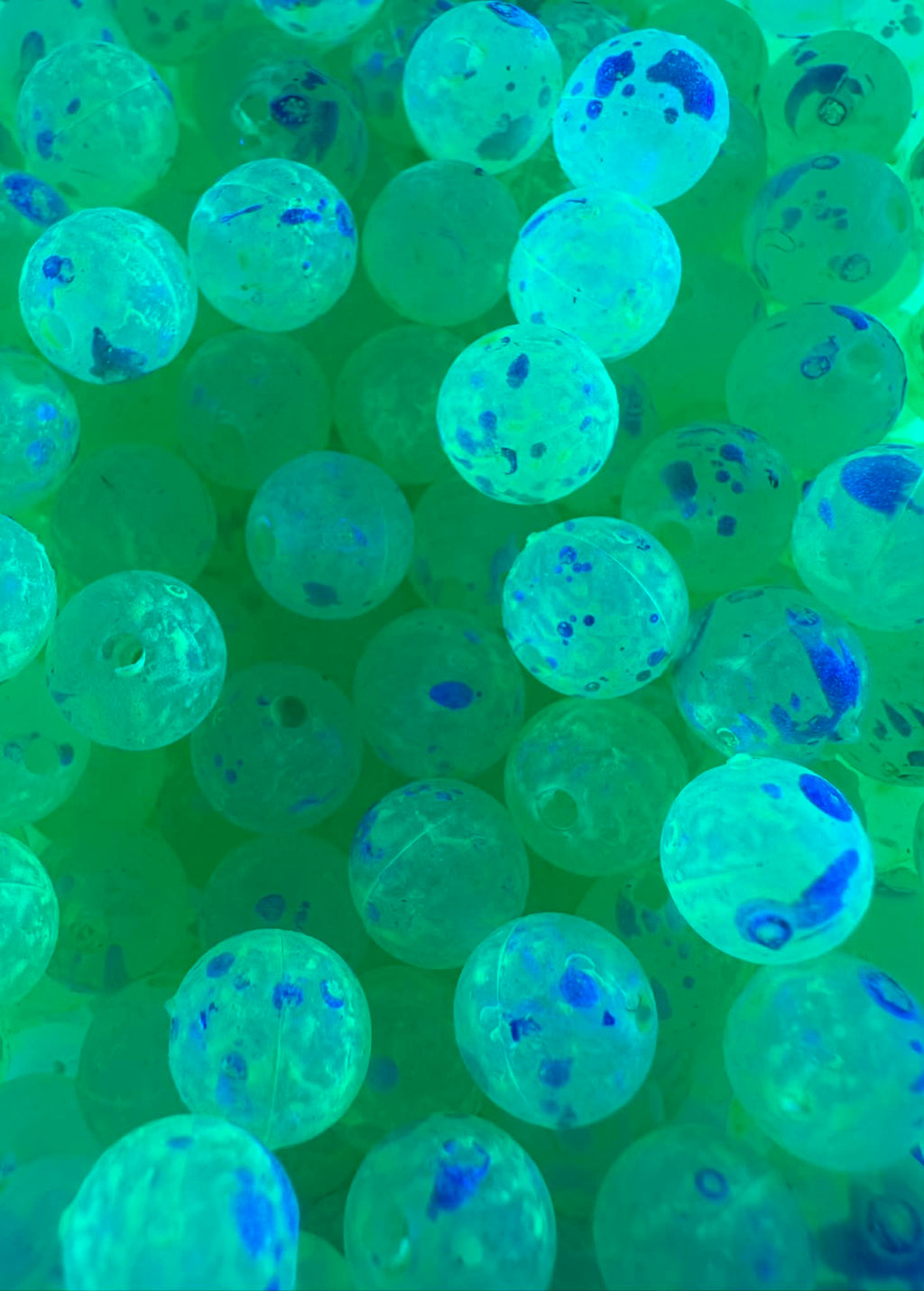 UV glow plastic fishing beads shown in blue-green light with dark speckling