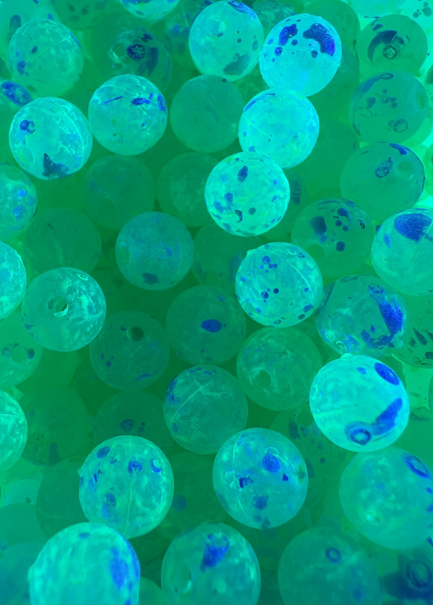 UV glow plastic fishing beads shown in blue-green light with dark speckling