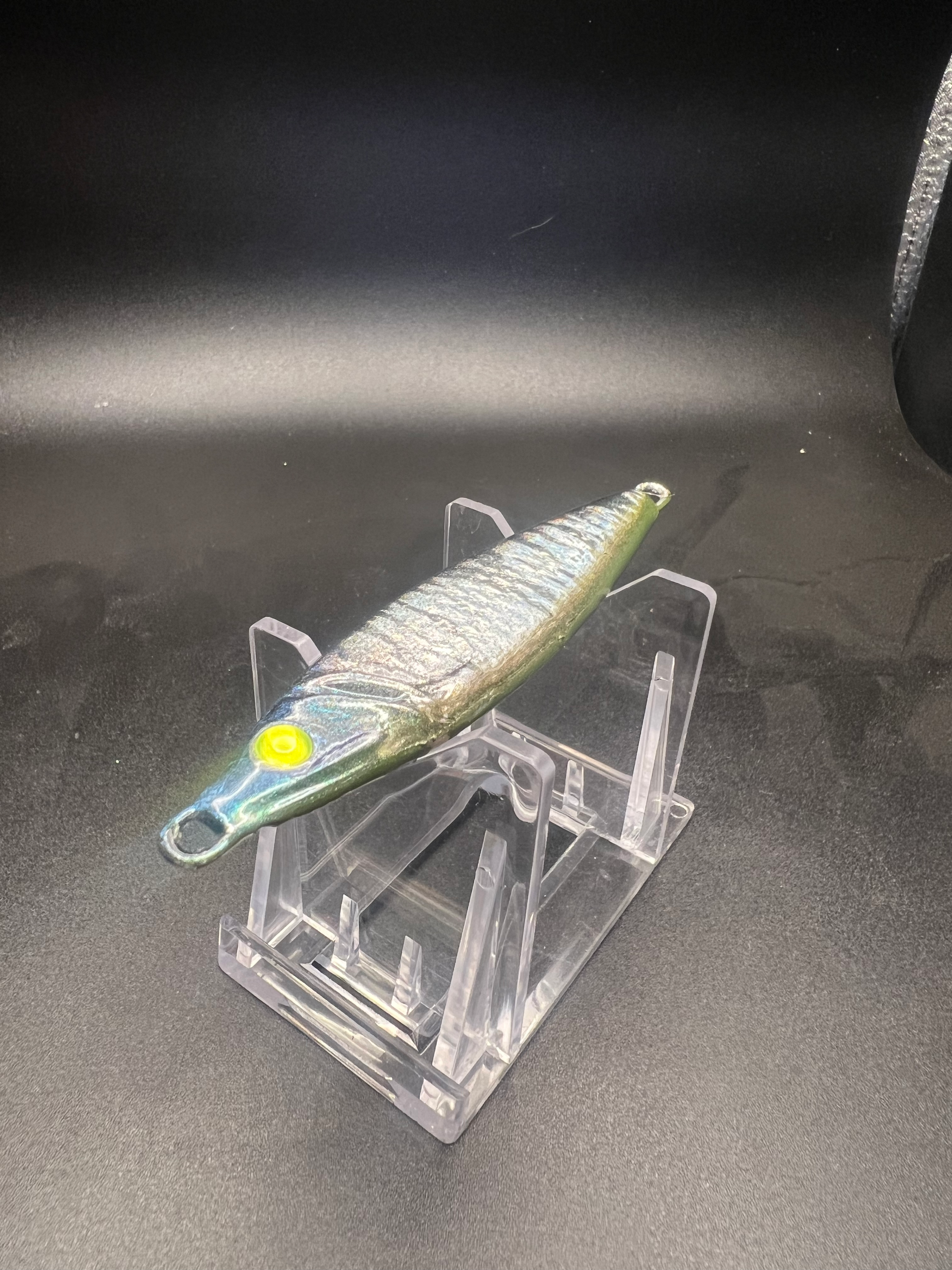 UV 2 oz jigging spoon with metallic green body, yellow eye, and side treble hook