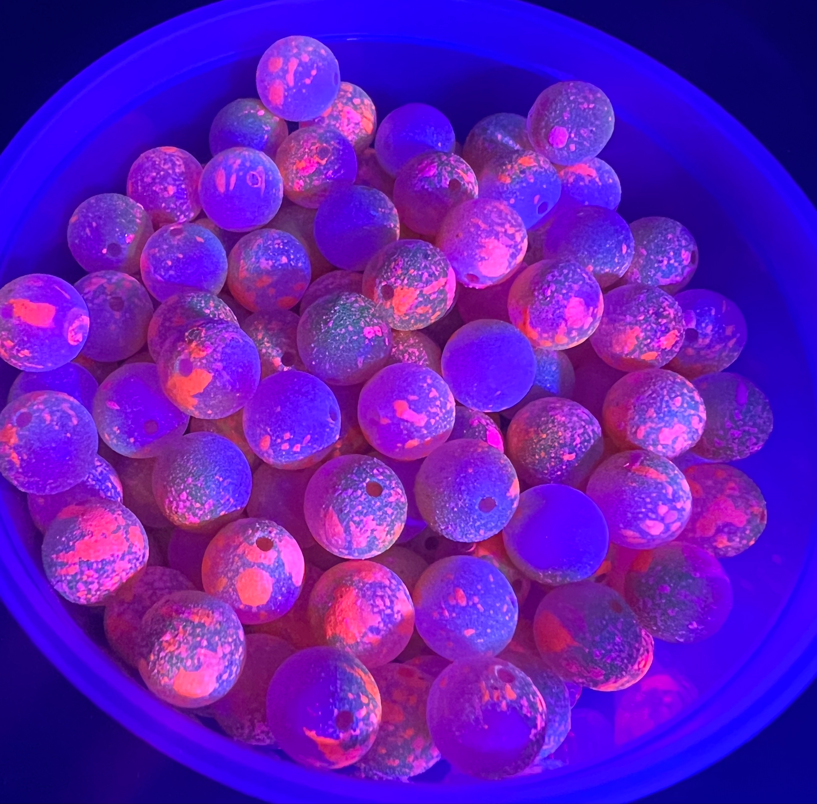 UV glow fishing beads in a blue tray, purple spheres with pink speckled highlights
