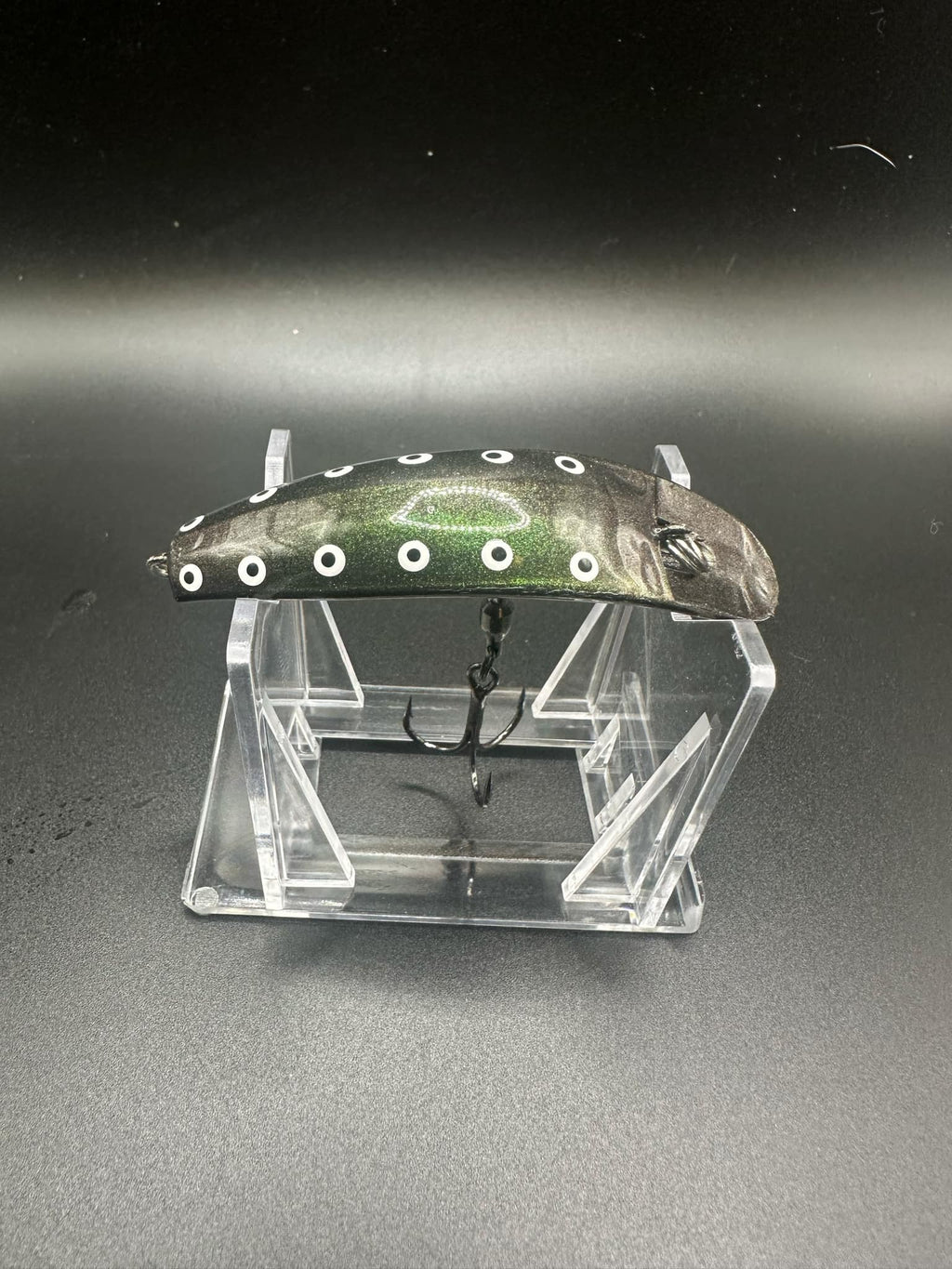 Jeremiah UV Swiftfish lure with dark body, white dot pattern, on clear display stand