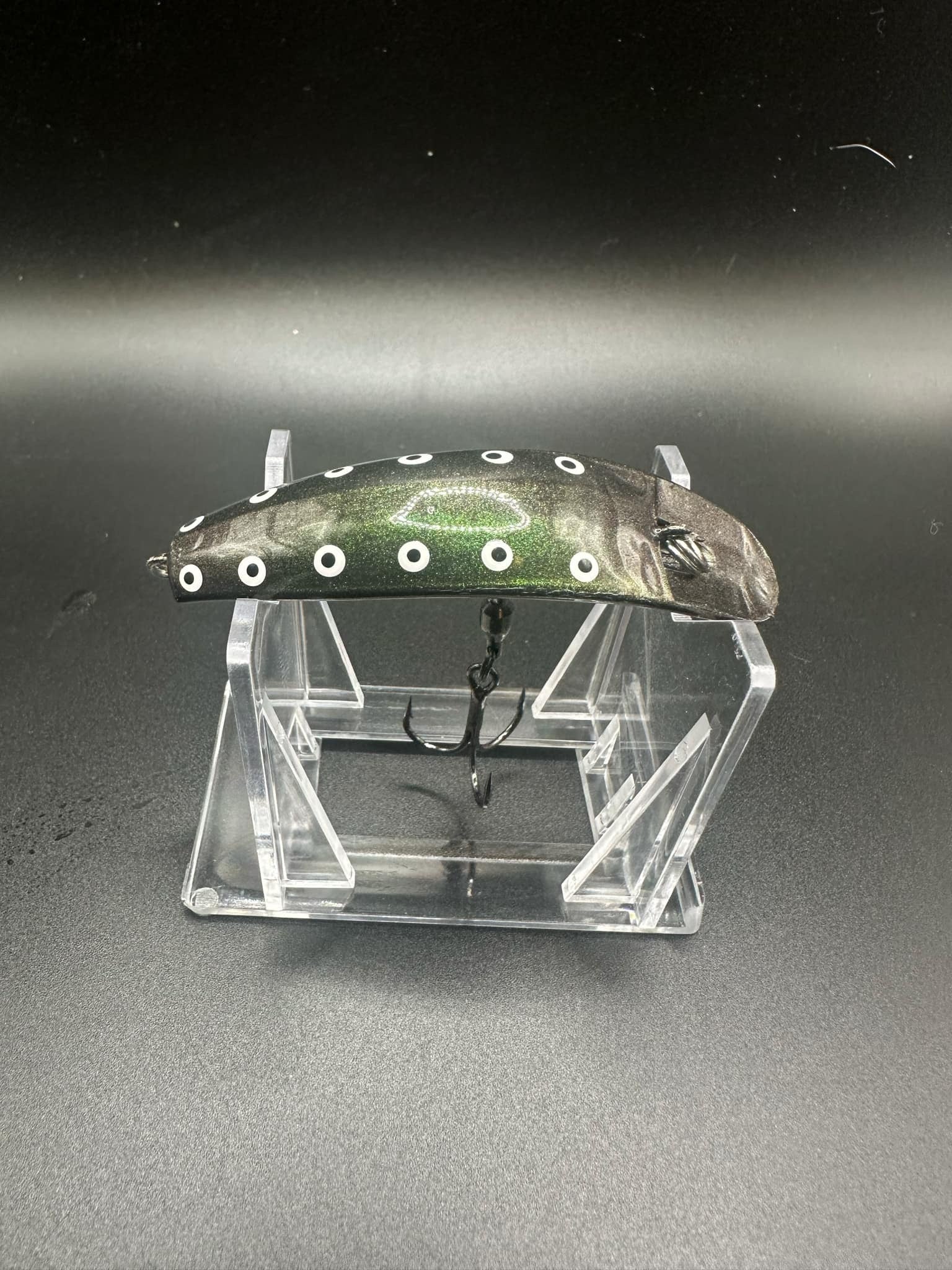Jeremiah UV Swiftfish lure with dark body, white dot pattern, on clear display stand