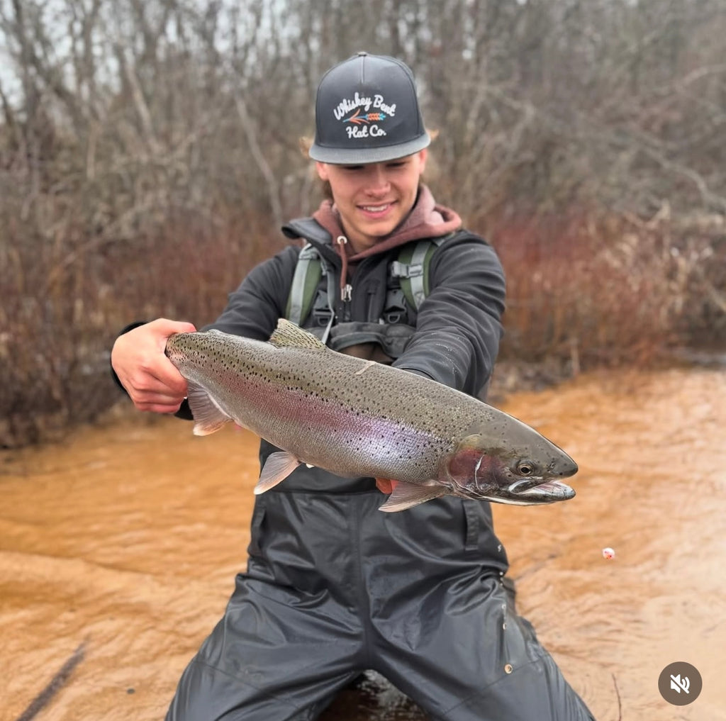 Caught steelhead trout held in hand beside a river