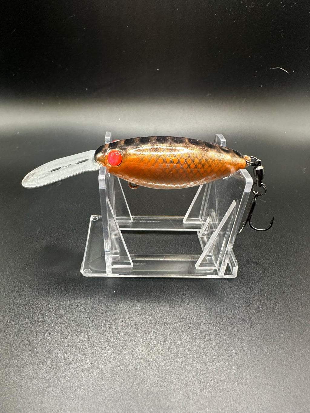 Orange Chromesicle fishing lure with red eye, silver lip, treble hooks on clear stand
